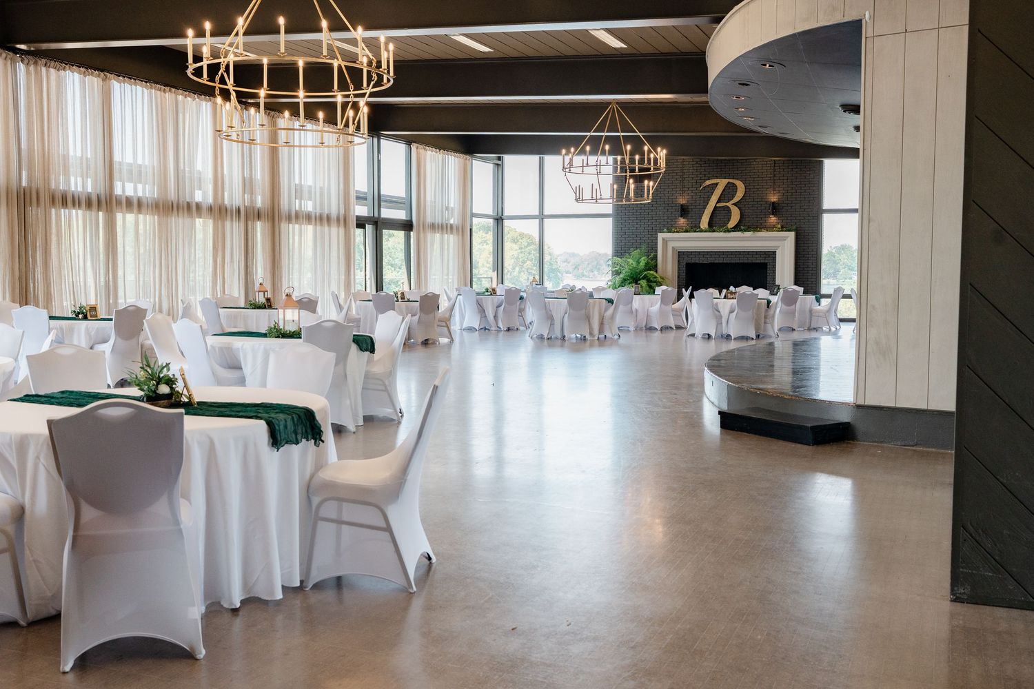 Elegant banquet hall with white-covered tables, gold chandeliers, and floor-to-ceiling windows creating an airy atmosphere.