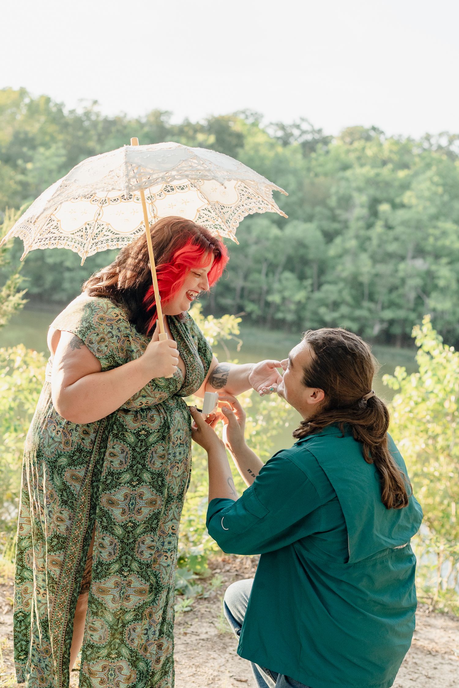 A couple poses playfully with a vintage lace parasol in a sunny outdoor setting during a romantic photoshoot.