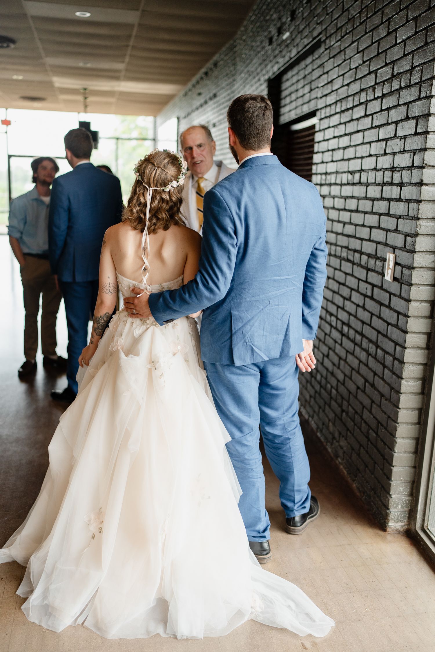 Wedding party walks through a modern hallway with black brick walls and natural lighting.
