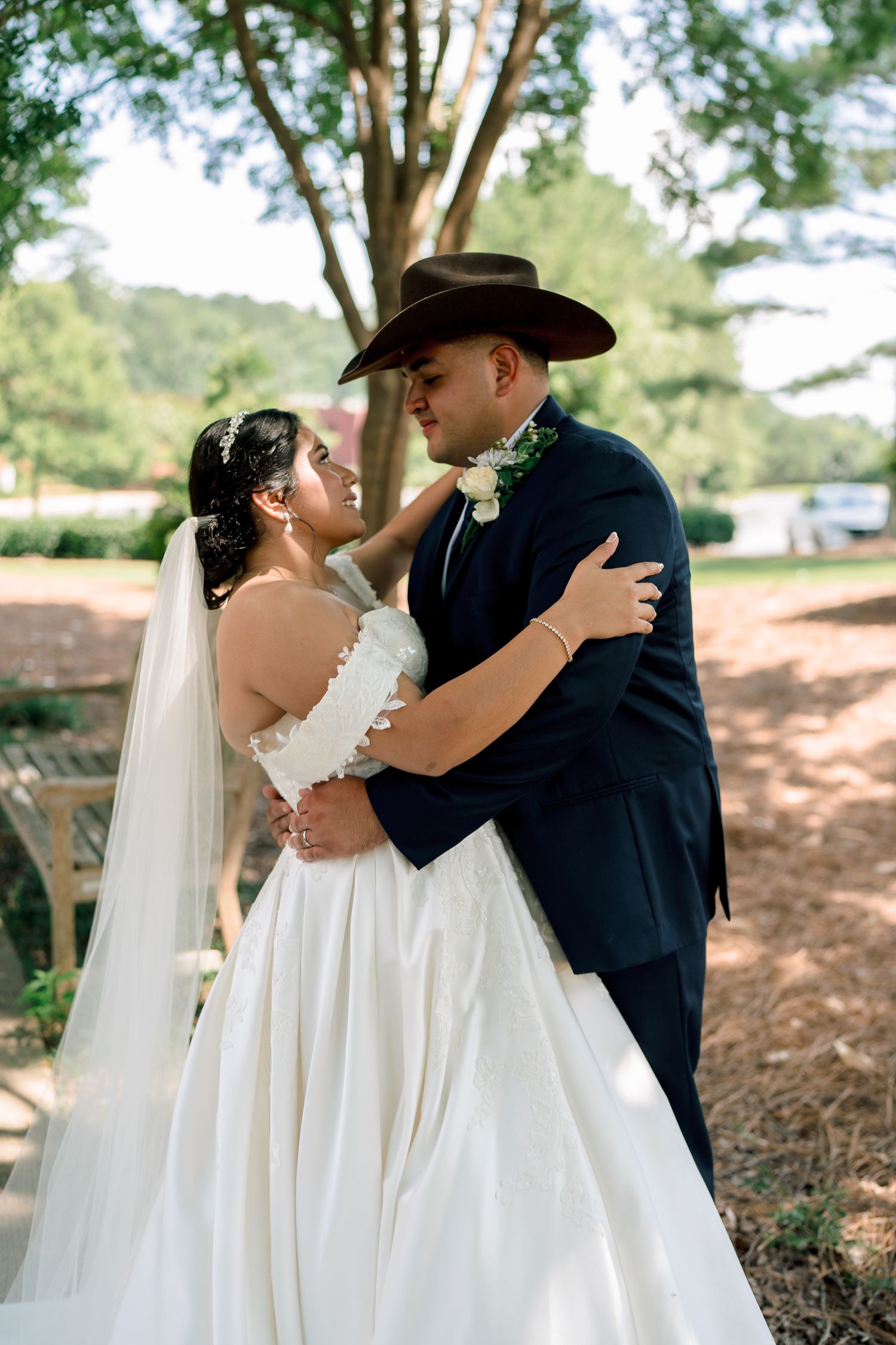 A couple shares romantic kisses in a wooded outdoor setting, with the bride in white and groom in navy blue.