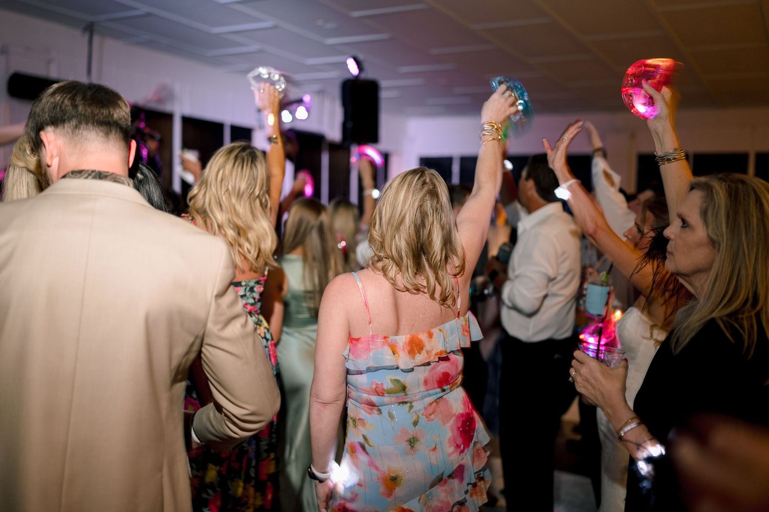 Guests dancing and celebrating at a lively wedding reception with colorful lights and festive atmosphere.