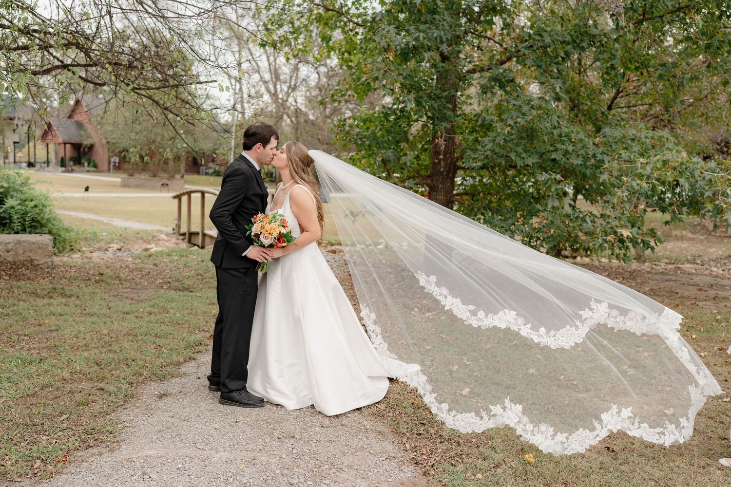 A couple shares a romantic moment outdoors with a flowing white veil creating an artistic silhouette against nature.