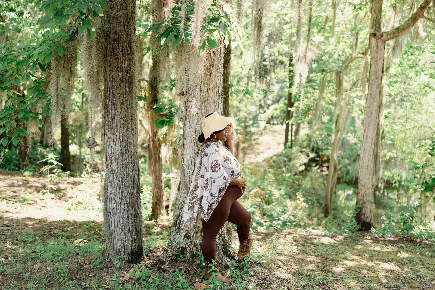 Figure in white patterned poncho and brown pants strikes a pose among forest trees.