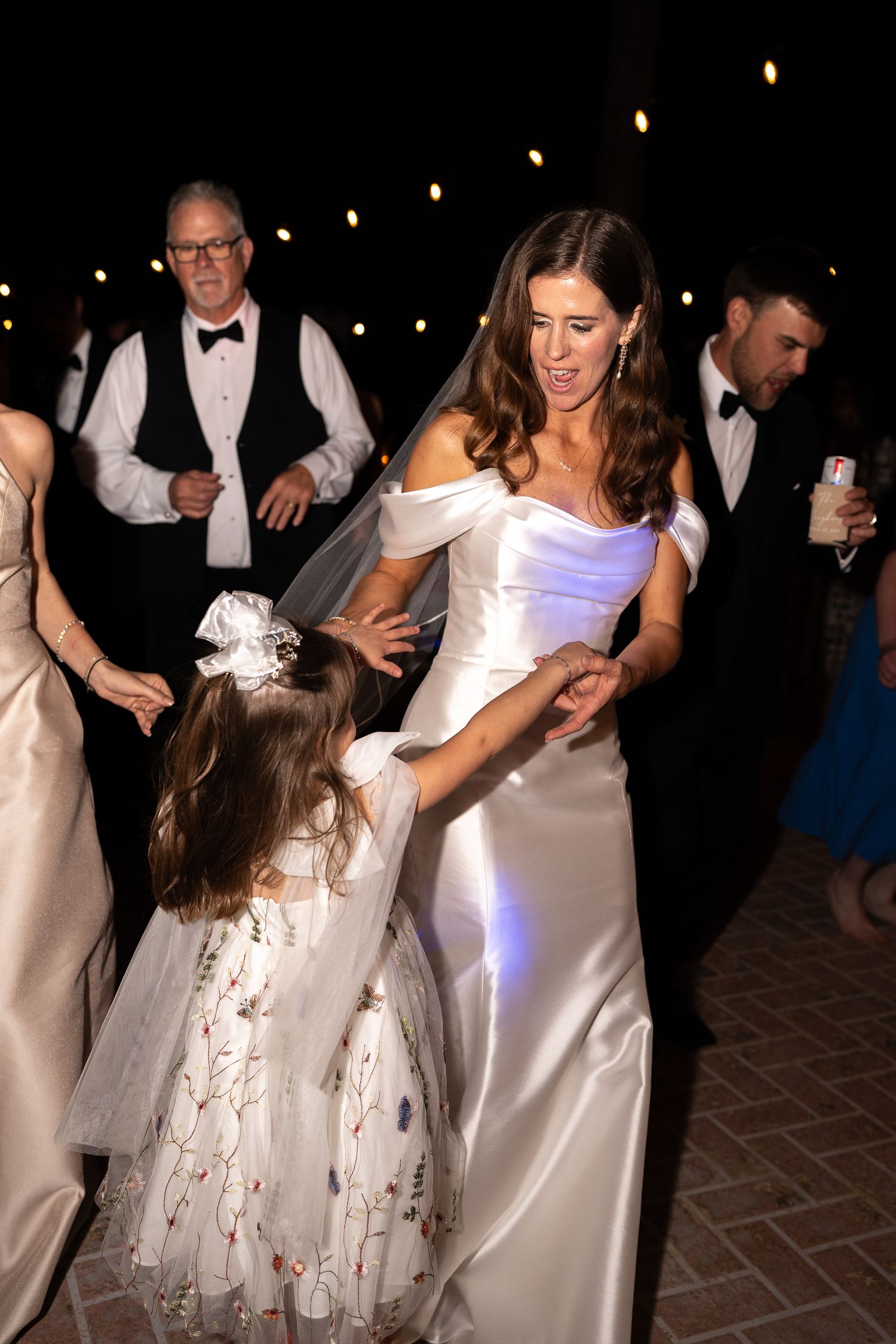 Wedding party members in white dresses dance together during nighttime celebration.