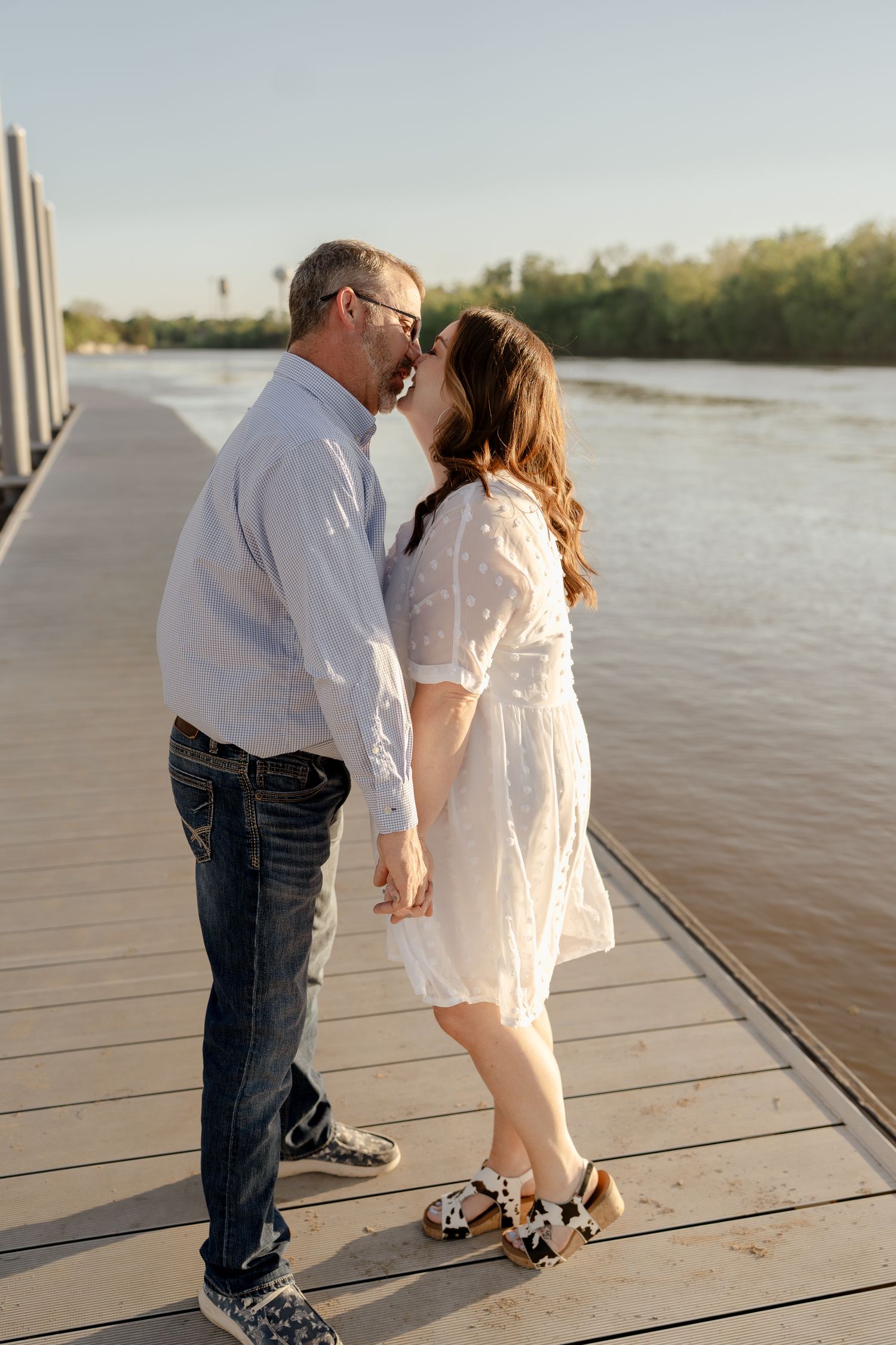 A couple interacts playfully on a wooden pier during a golden hour photoshoot.