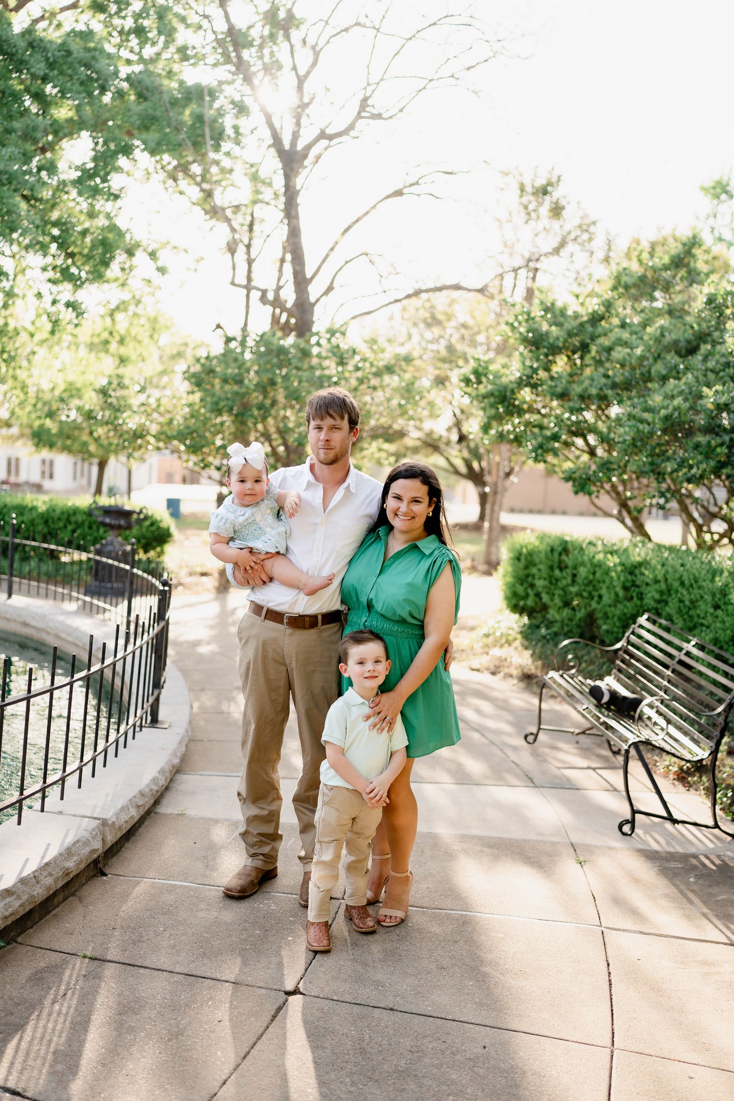 Family members interact playfully during outdoor photo shoot along tree-lined concrete path.