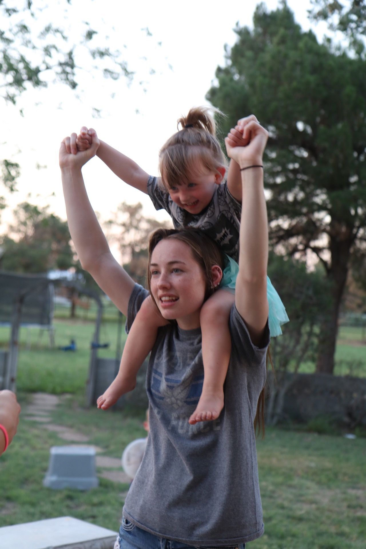 A joyful shoulder ride outdoors with arms raised in celebration.
