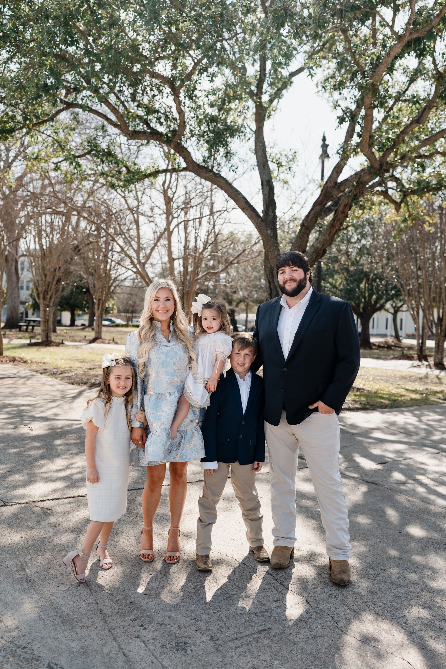Family group poses on path under oak trees wearing coordinated spring outfits.