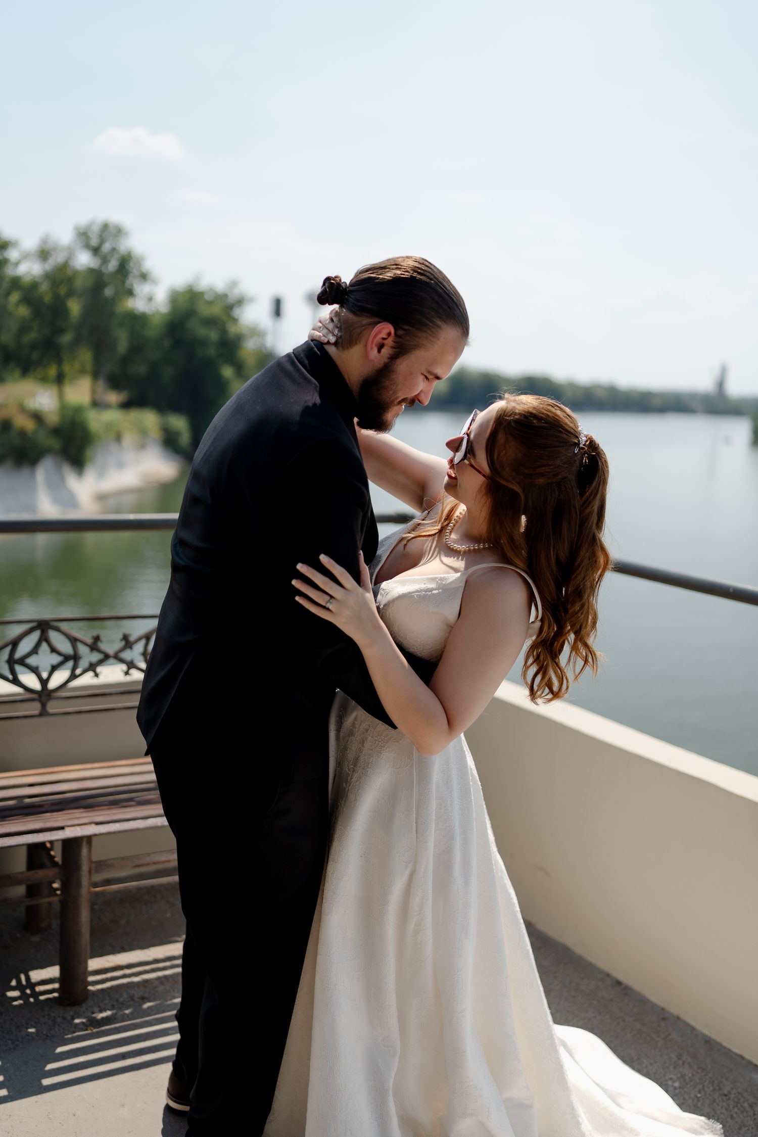 A couple shares a romantic kiss on a waterfront balcony in a series of candid wedding photos.