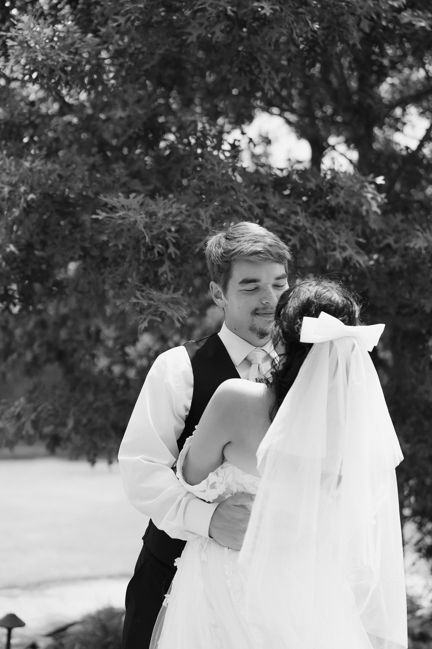 Black and white photo of groom tenderly holding bride in a romantic outdoor wedding portrait.