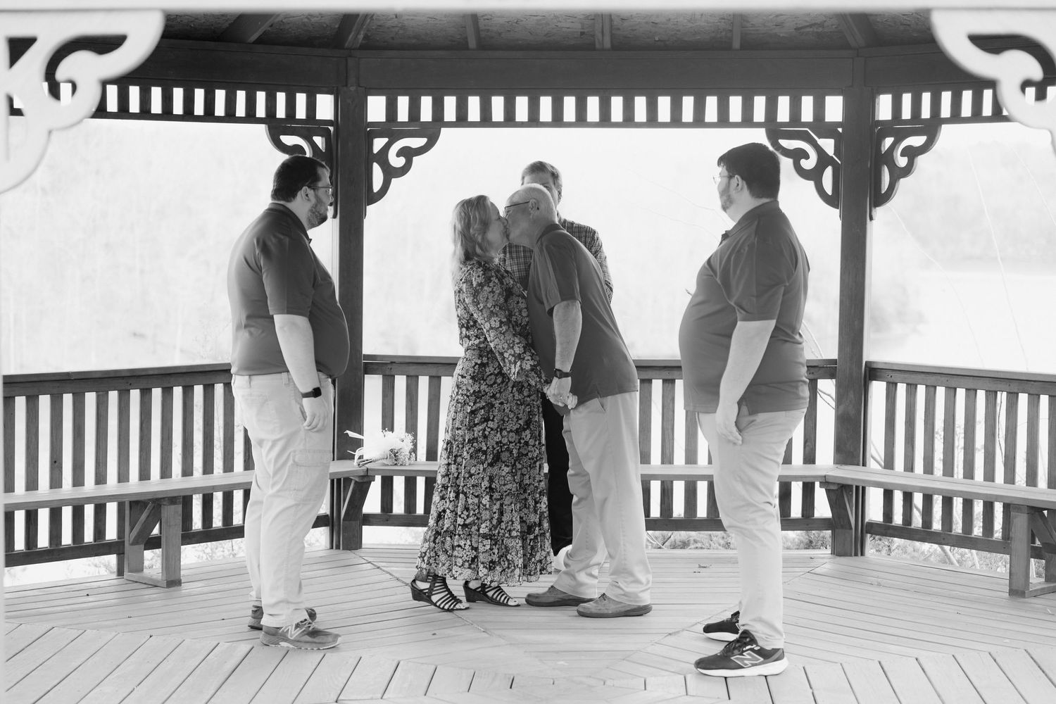 Black and white photo of a small wedding ceremony group gathered inside a wooden gazebo.