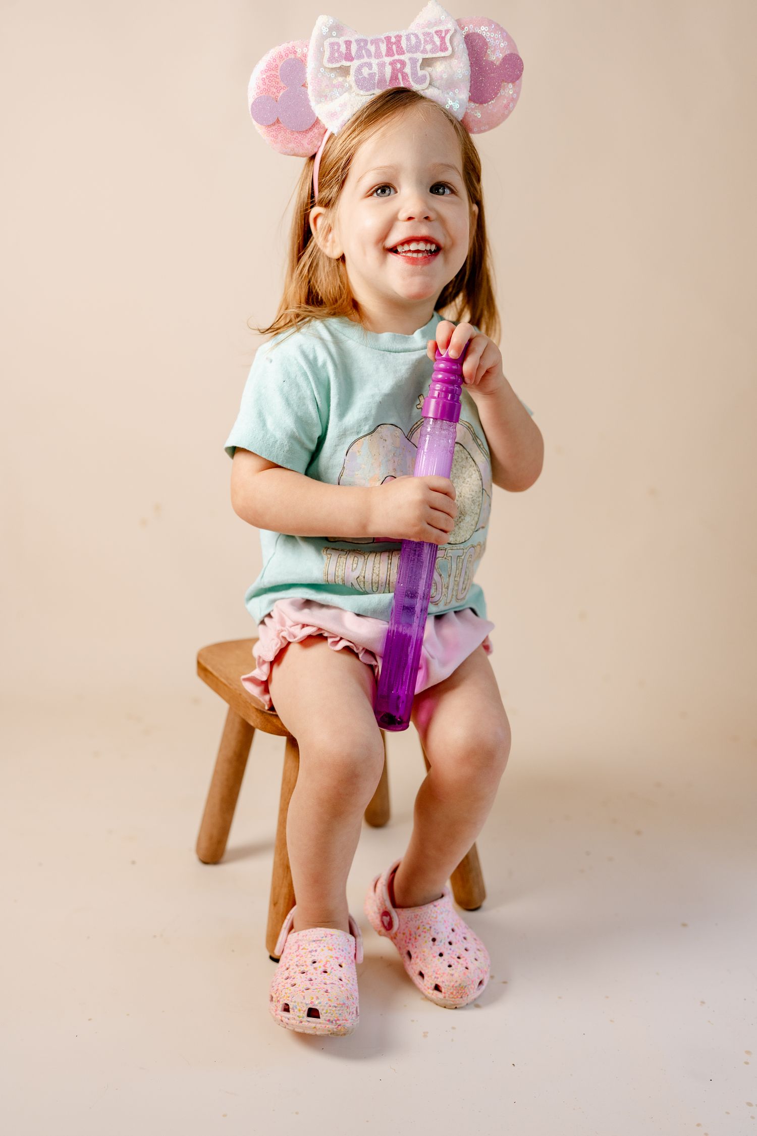 A wooden stool and purple bubble wand create a playful scene against a neutral backdrop.