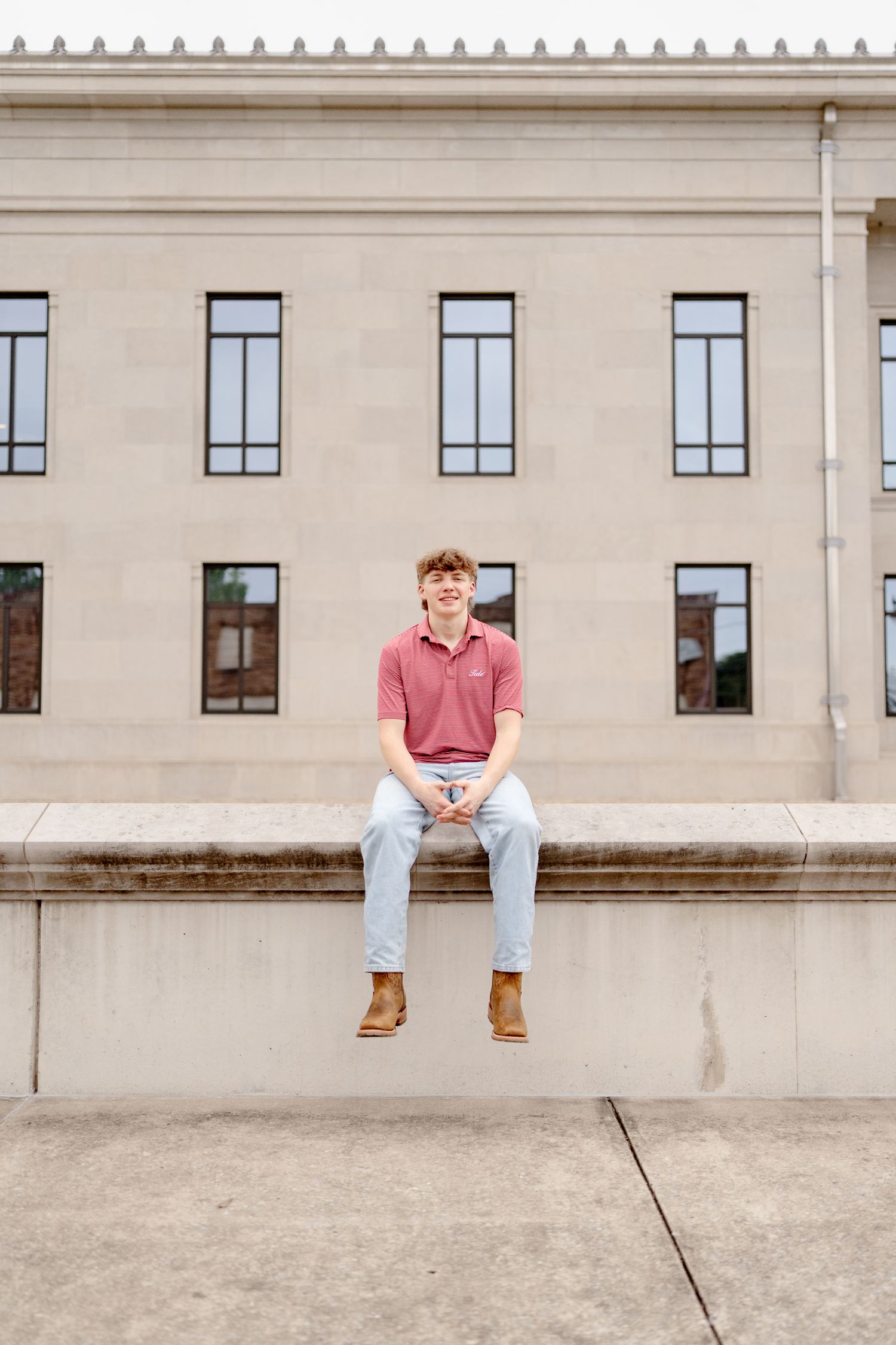 Someone sits on a concrete ledge outside a modern building with rows of windows.