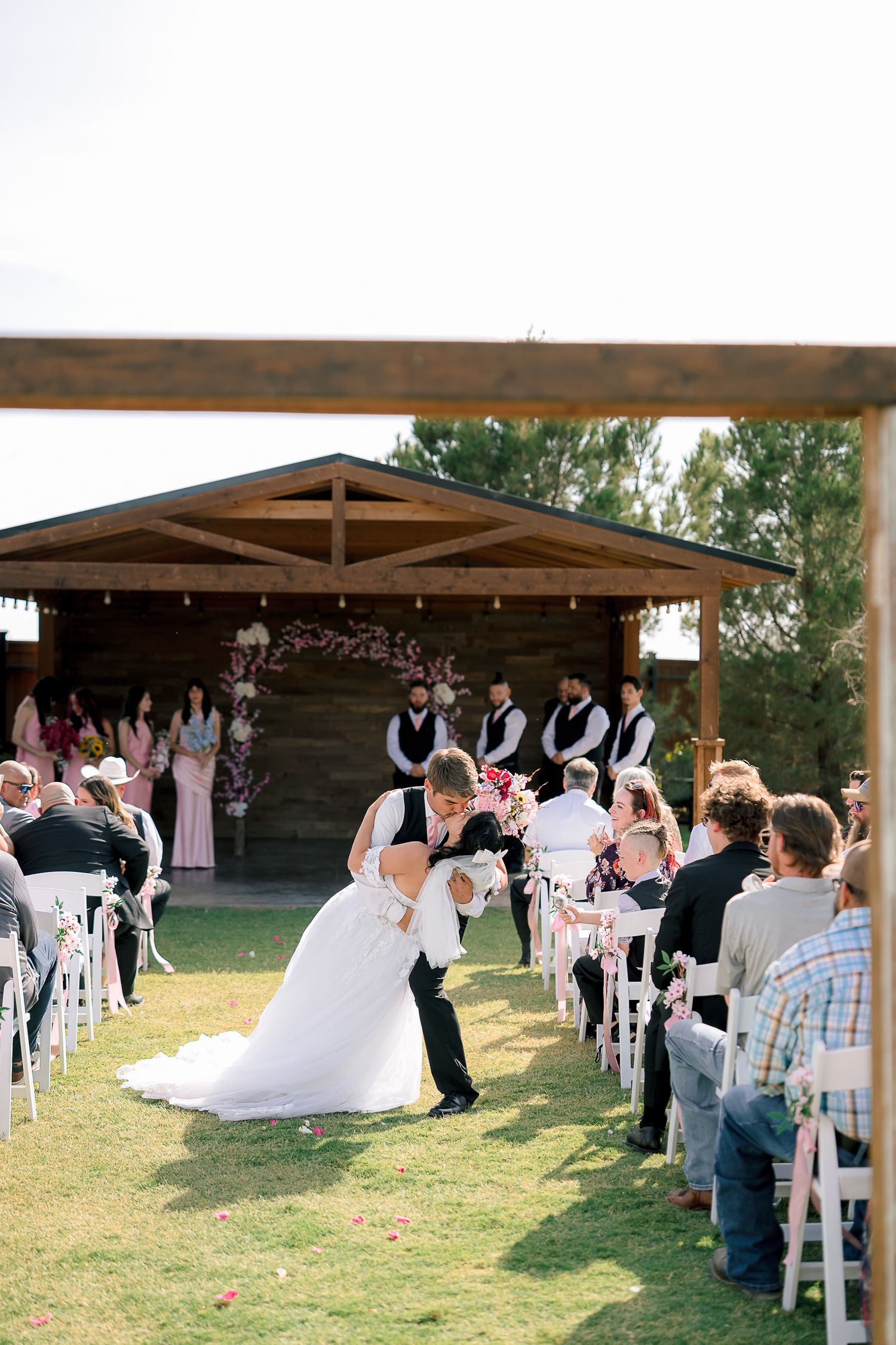 Groom dips bride in a romantic kiss at the end of the aisle during an outdoor wedding ceremony.
