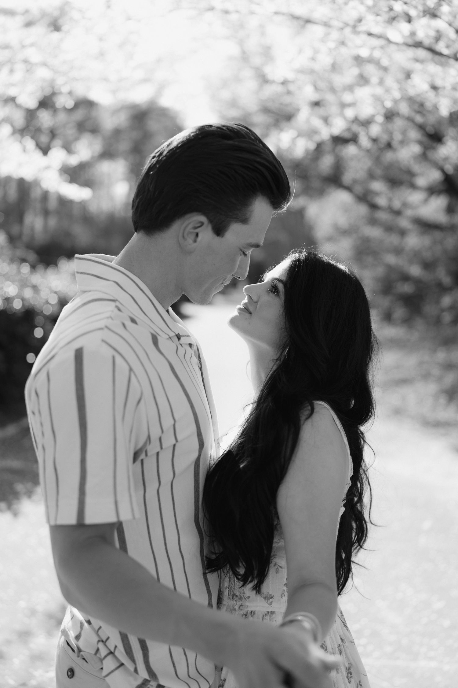 Black and white photo of a romantic couple almost kissing outdoors, surrounded by blossoming trees.
