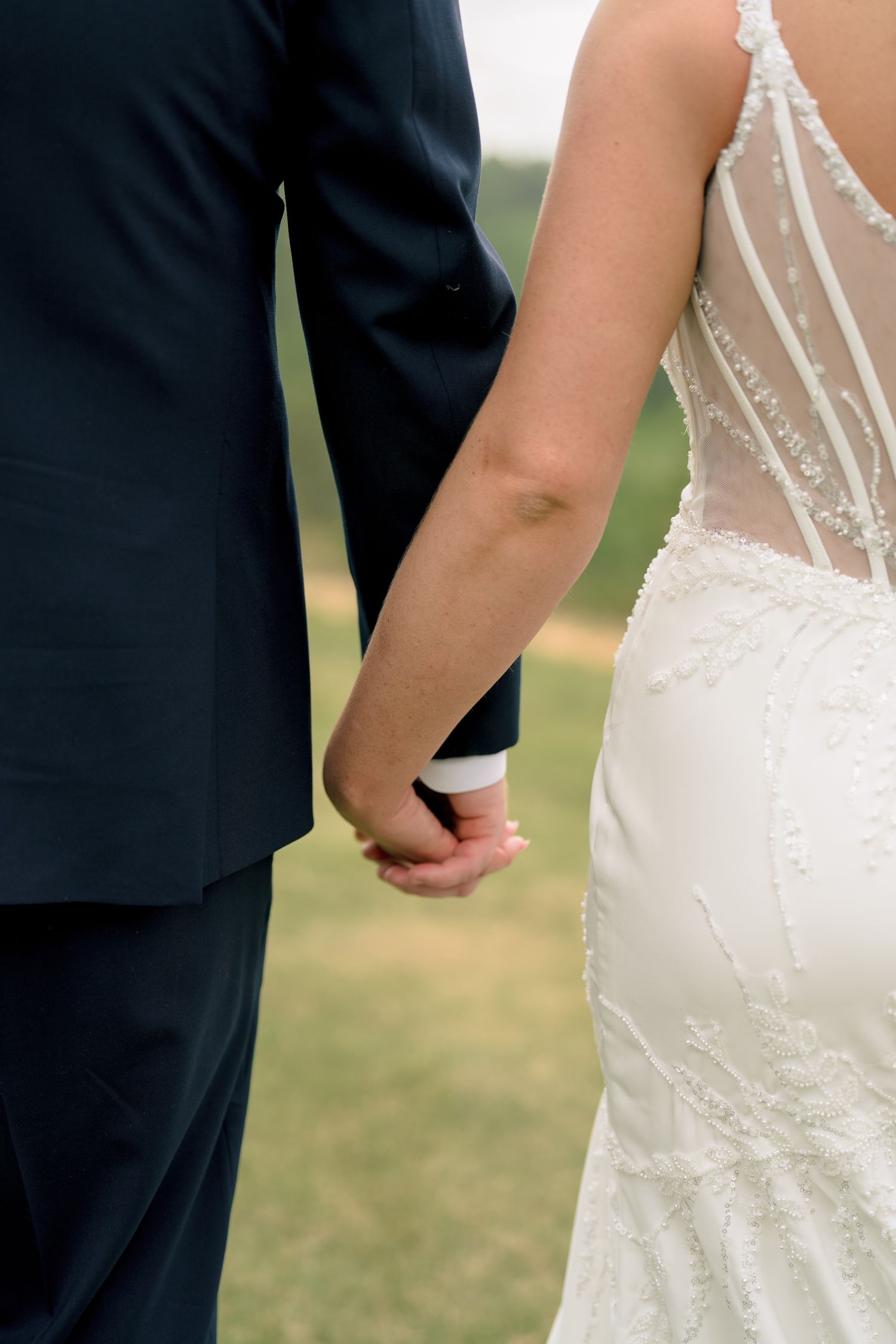 Bride and groom holding hands, showing back detail of lace wedding dress and navy suit.