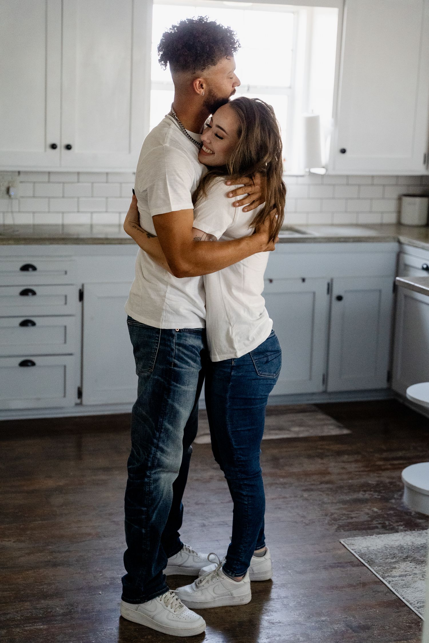 Couple embracing in bright white modern kitchen wearing casual attire.