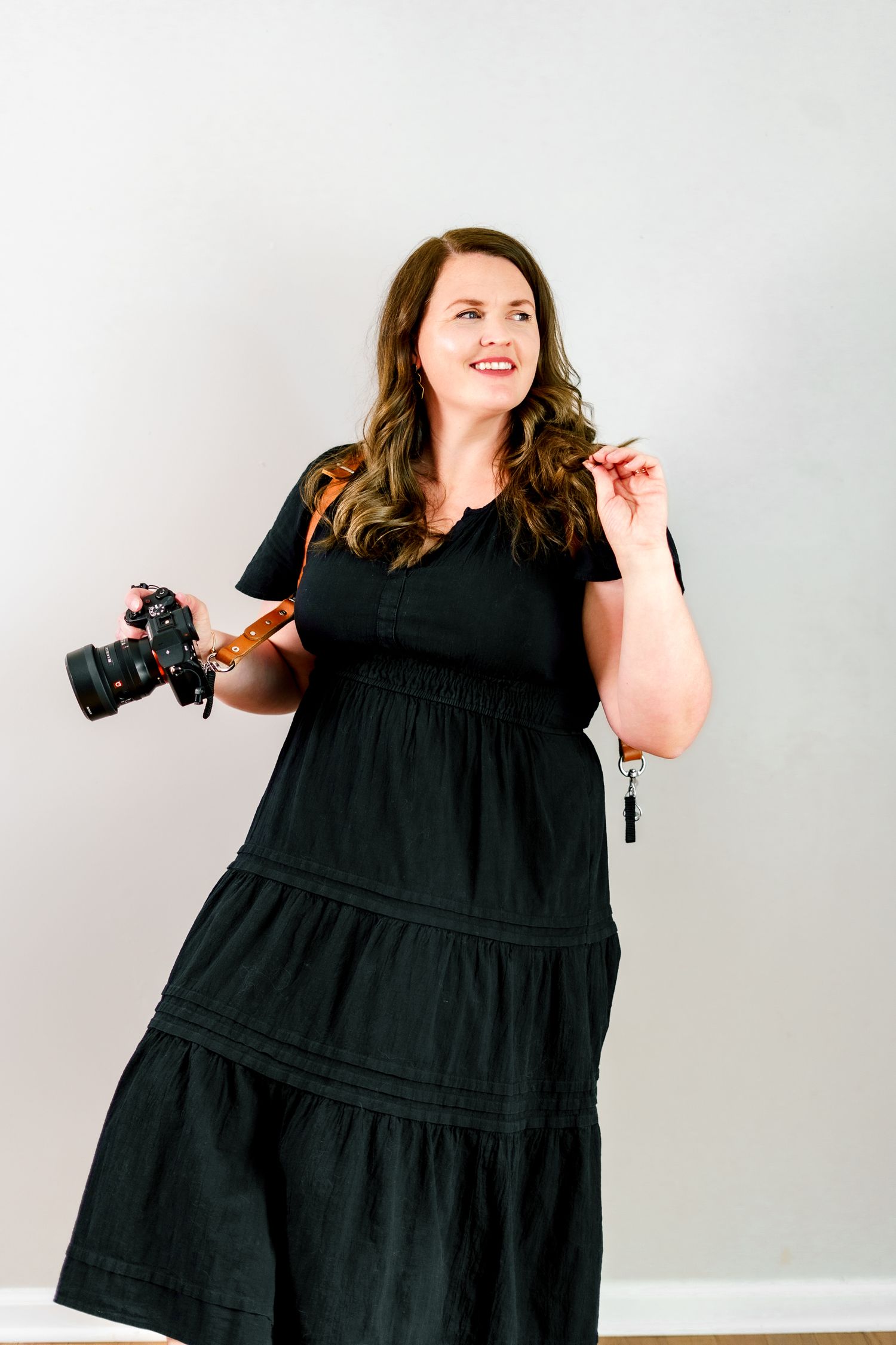 A photographer in a flowing black dress shows dynamic poses against a white background.