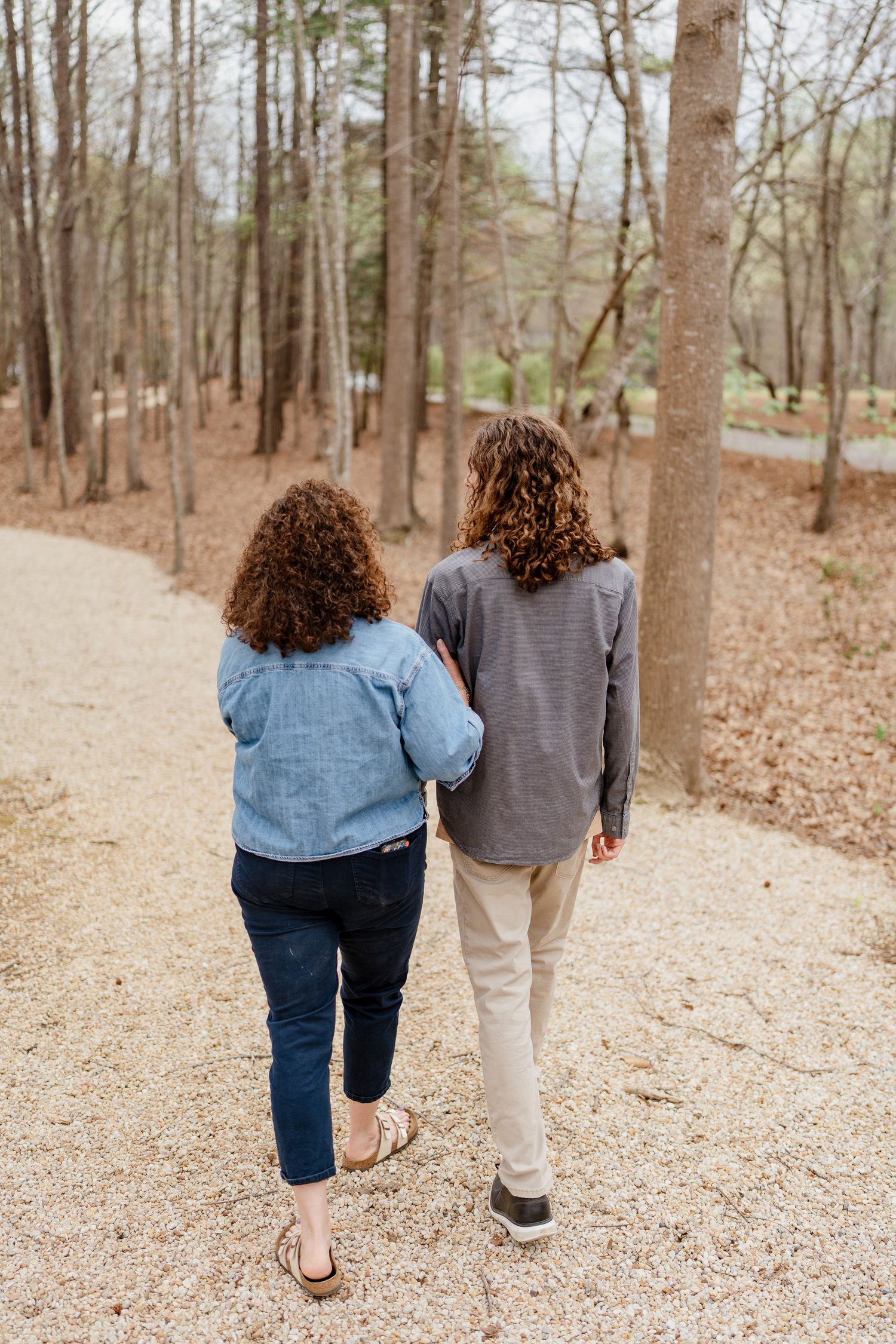 Two people walking away on a gravel path through a forest wearing casual clothes.