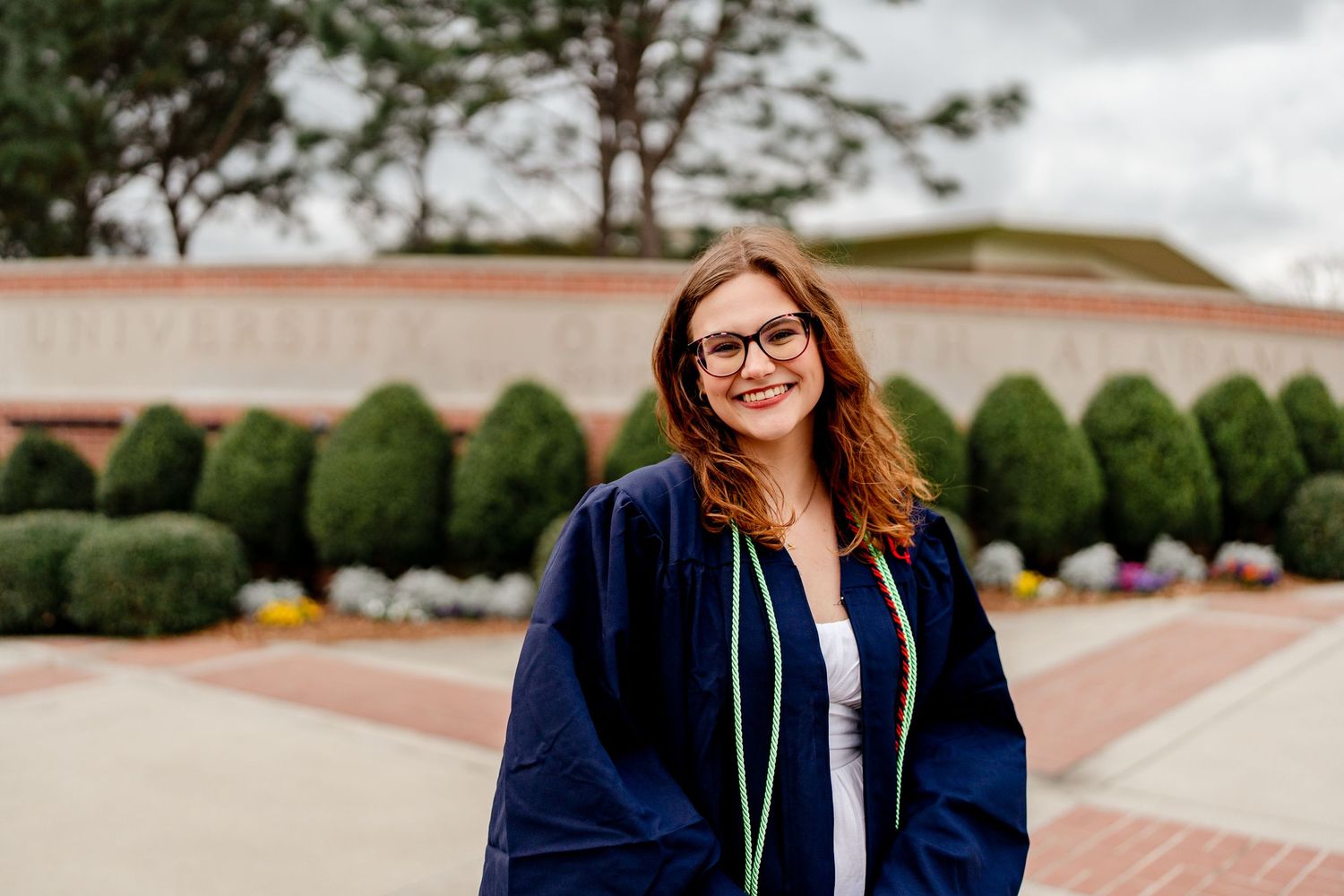 Graduate celebrating with diploma and navy gown on campus steps.