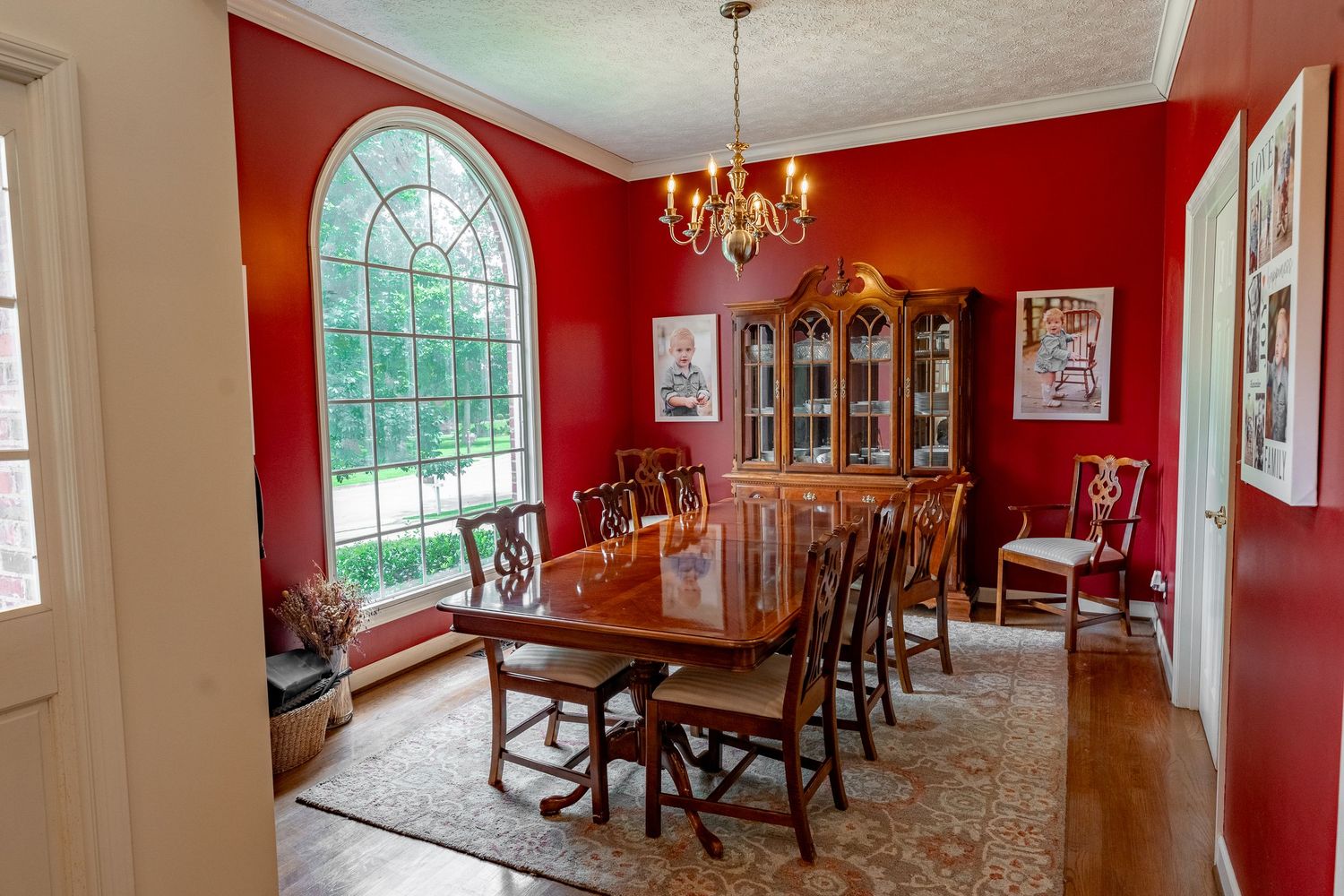 Formal dining room with bold red walls, arched window, crystal chandelier and traditional wooden furniture.