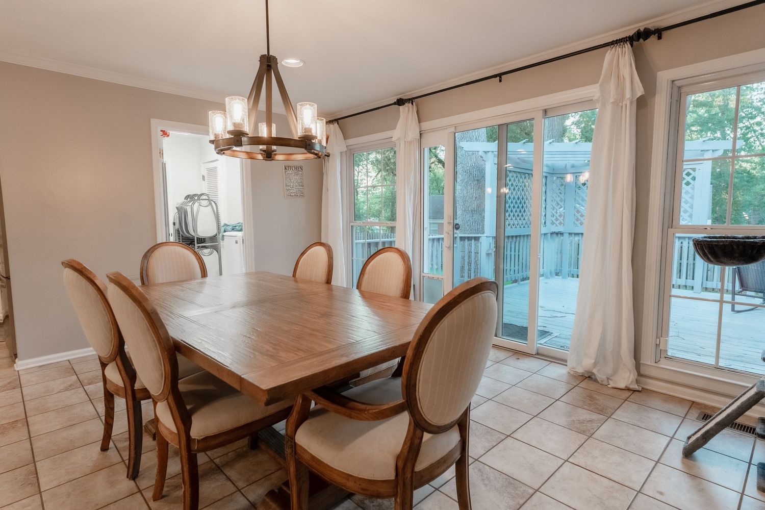 Bright dining area with white tile floors, beige walls, and large windows showcasing natural light.