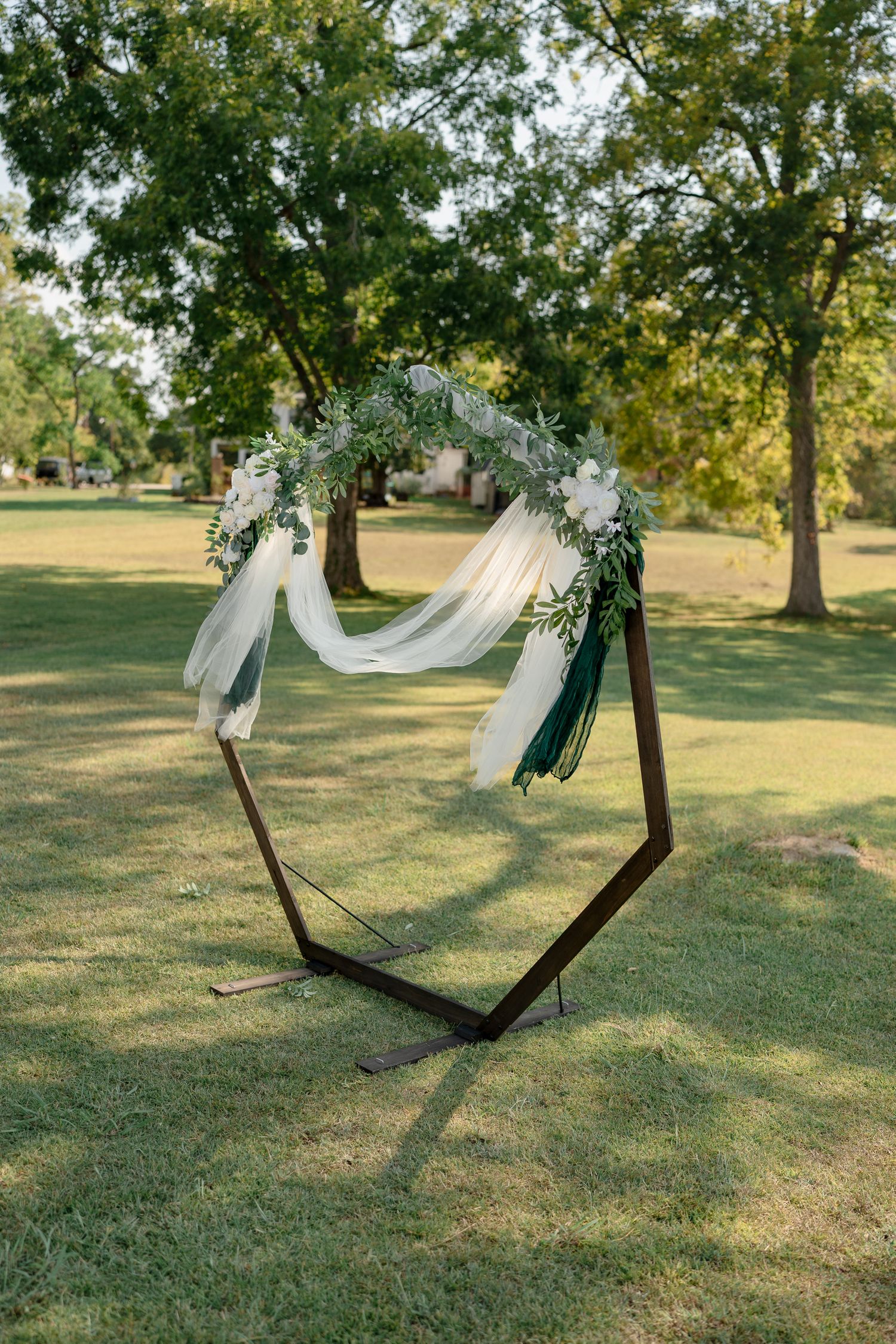 Wooden hammock decorated with white fabric and floral arrangements in an outdoor garden setting.
