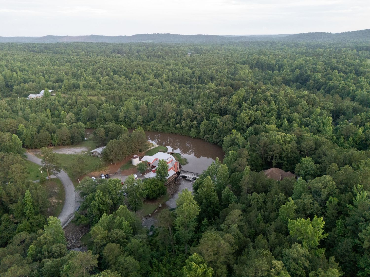 Aerial drone view of rustic barn wedding venue surrounded by dense forest and green trees.