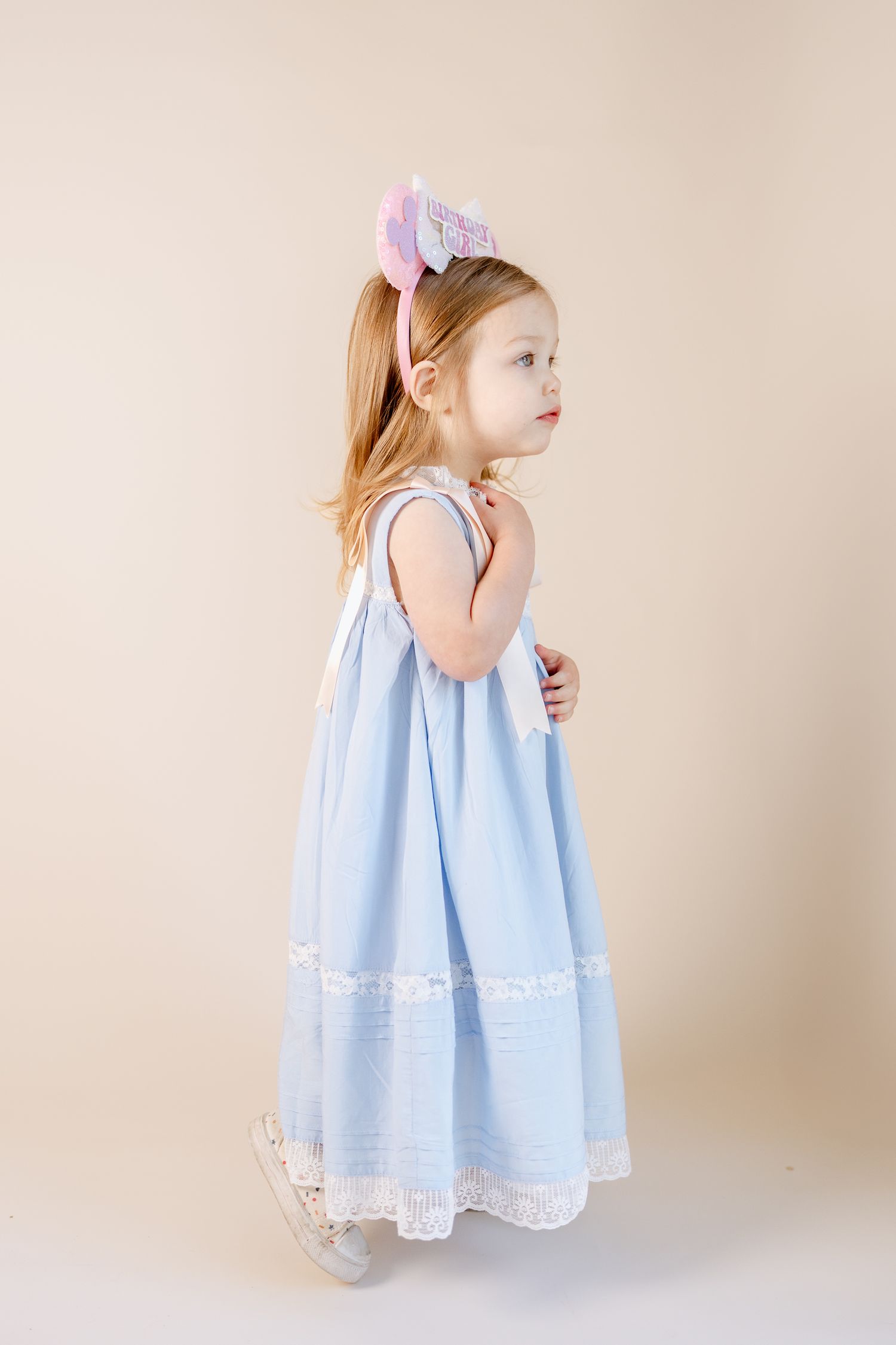 A delicate light blue dress with white lace trim is captured in a minimalist studio setting.