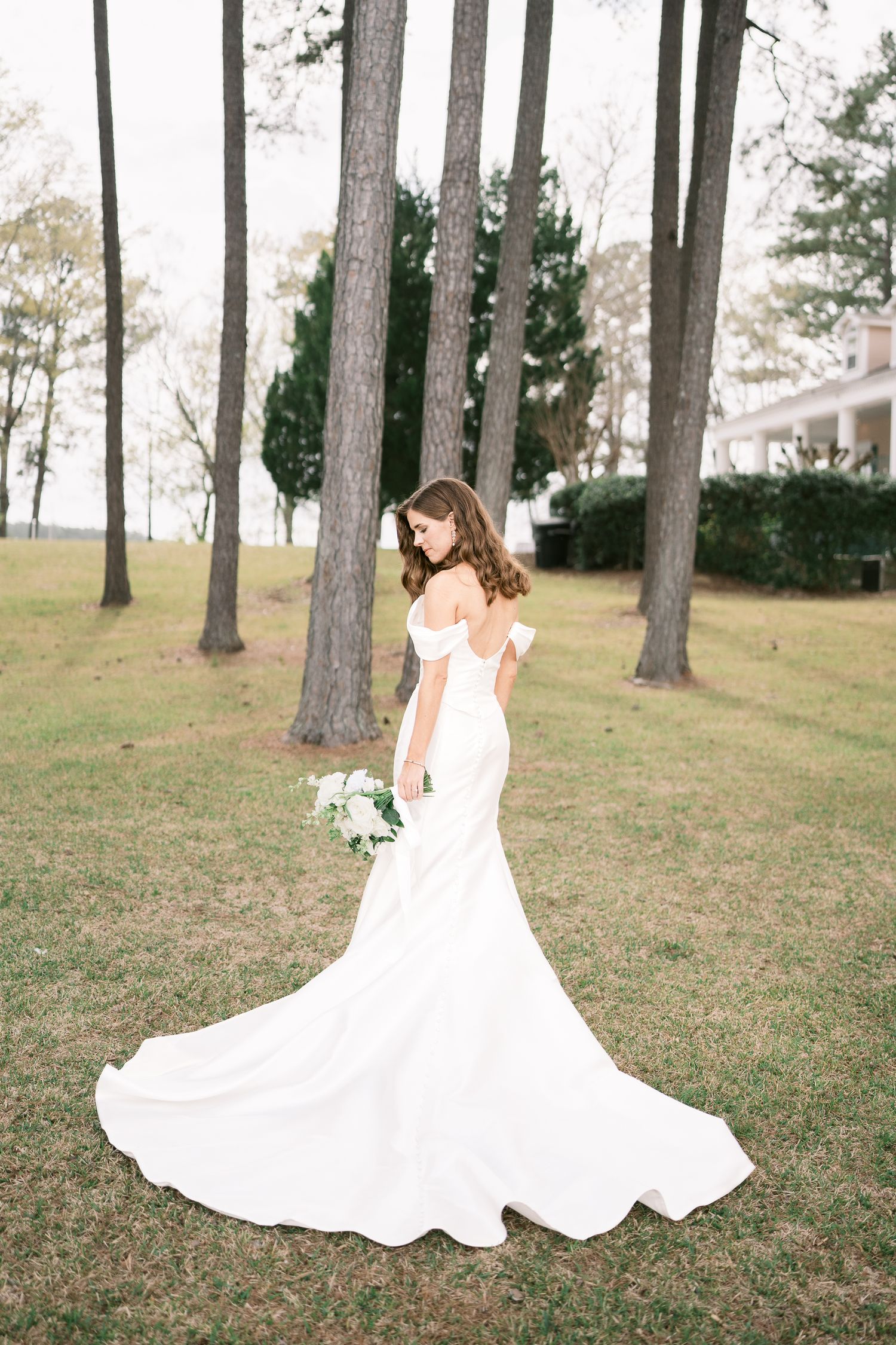 Bride in fitted mermaid gown with dramatic train poses among tall pine trees.