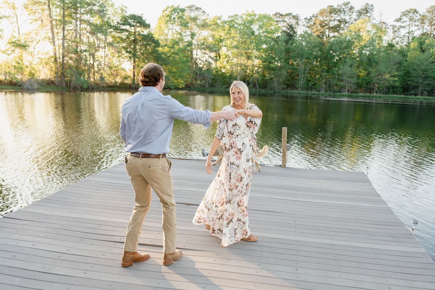 A couple dances together on a wooden dock overlooking a serene lake at sunset.