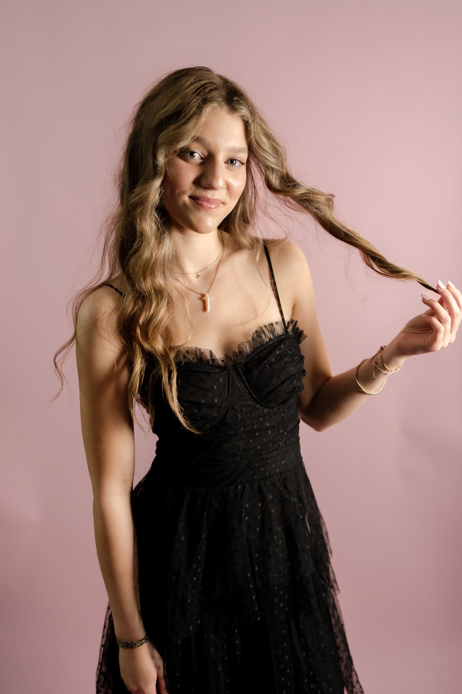 Playful fashion poses highlight a flowing black dress against a pink backdrop.