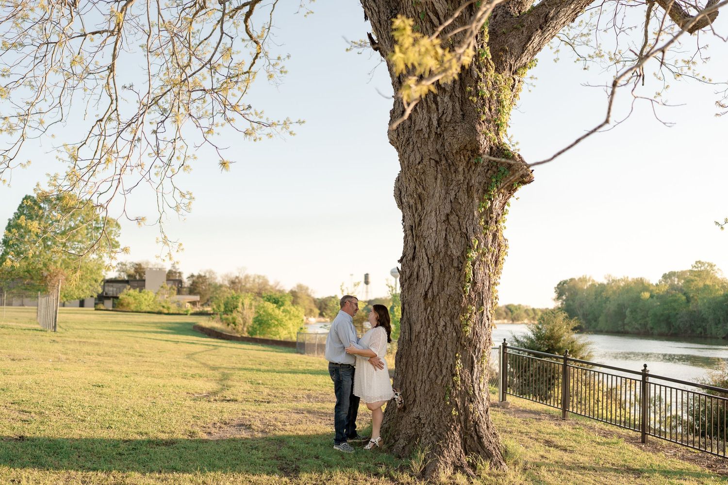 A couple standing beneath a large tree with a river view in the background.