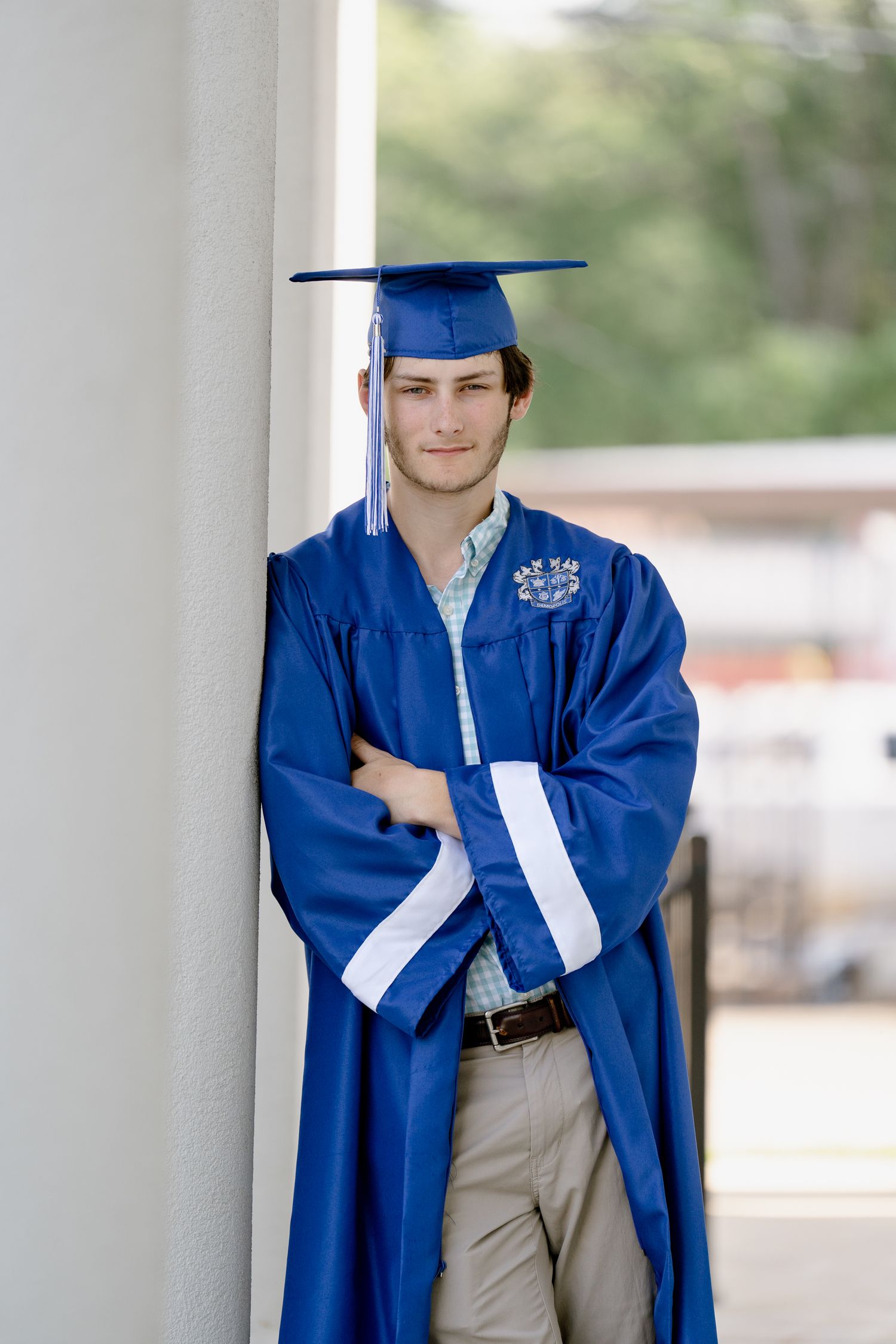 Graduate in blue and white academic regalia poses against white column.