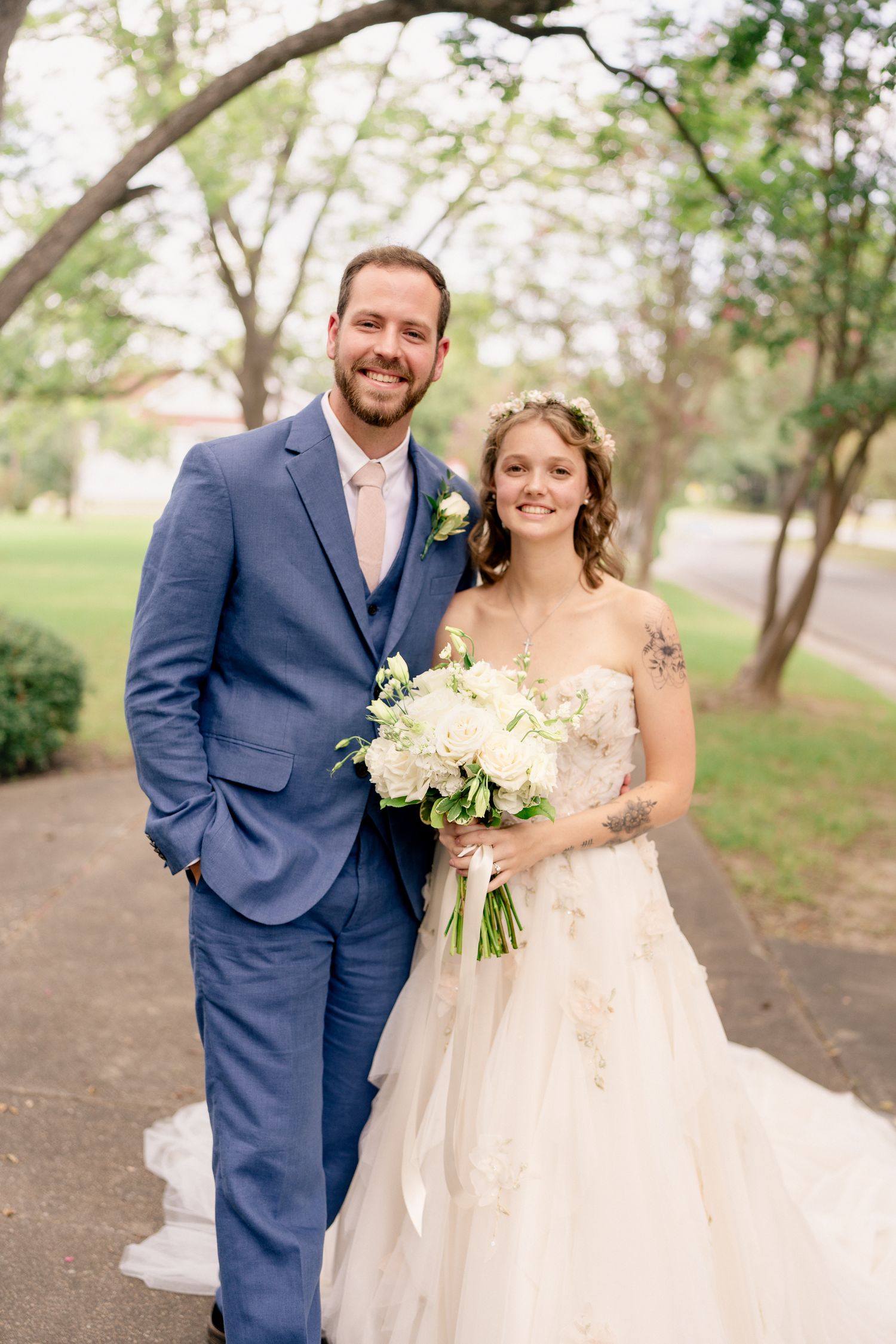 A wedding couple poses together outdoors with white flowers against a natural backdrop.