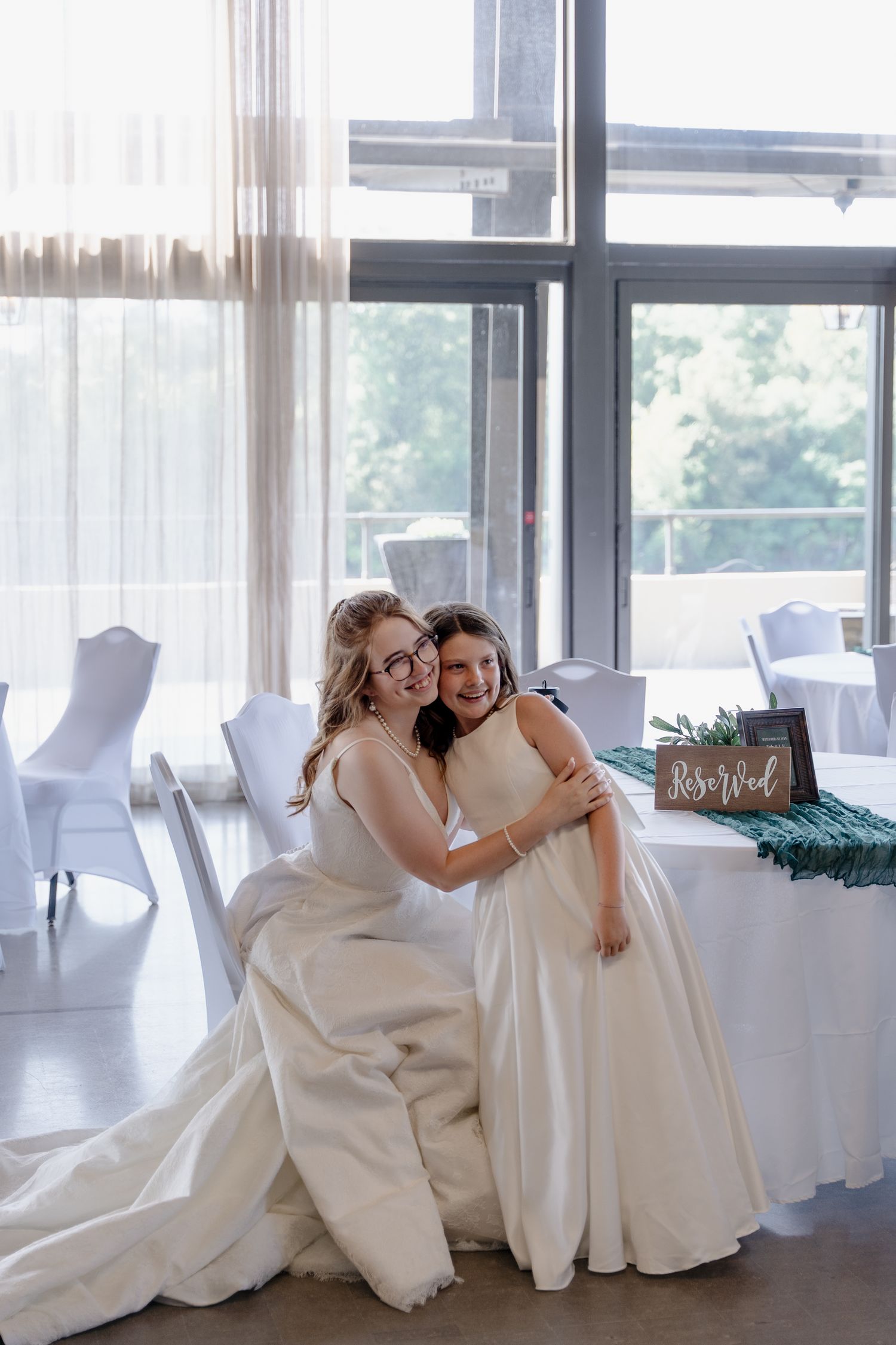 Wedding venue interior with white chairs and sheer curtains by large windows.