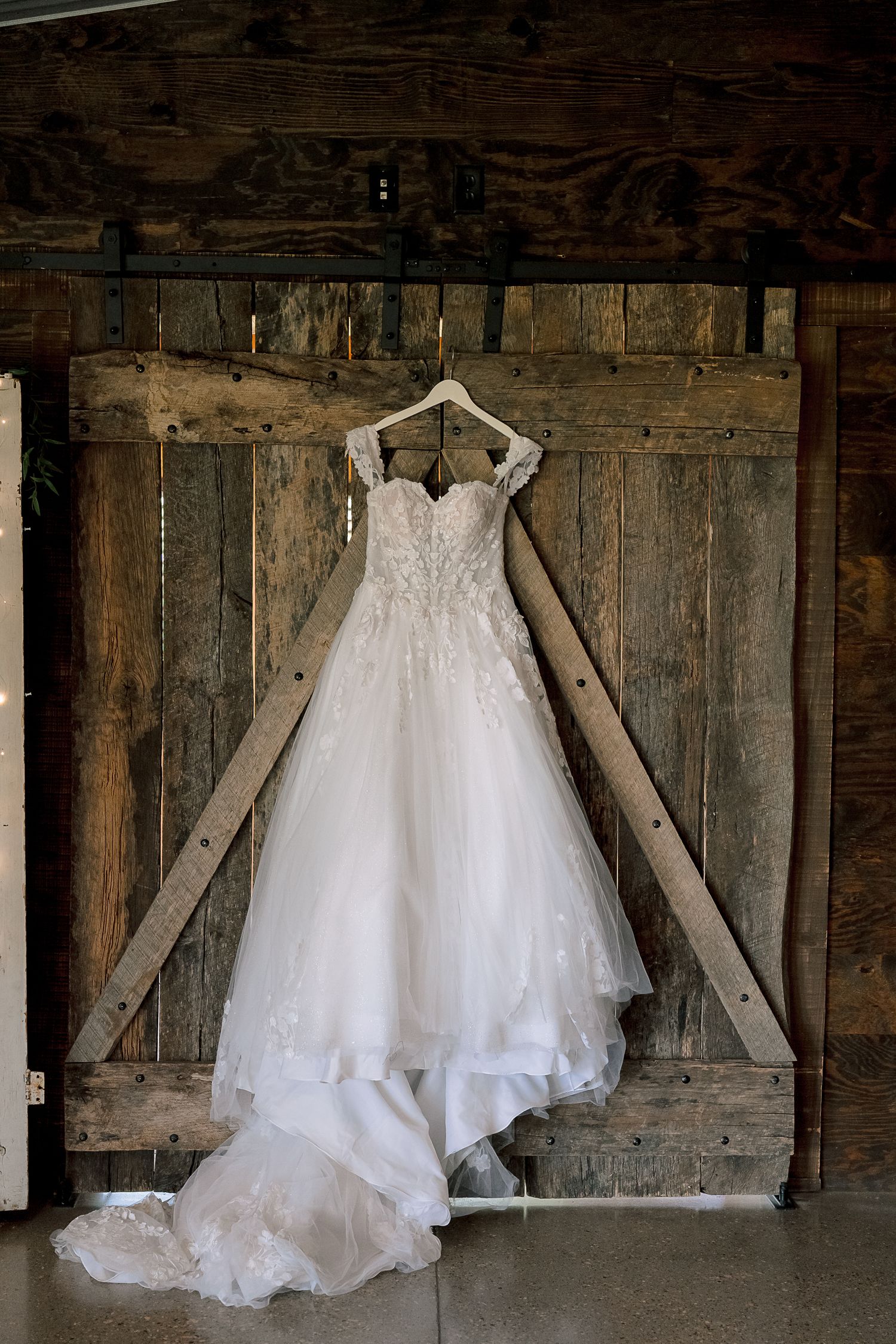 Elegant white lace ballgown wedding dress hanging on rustic barn wood sliding doors.