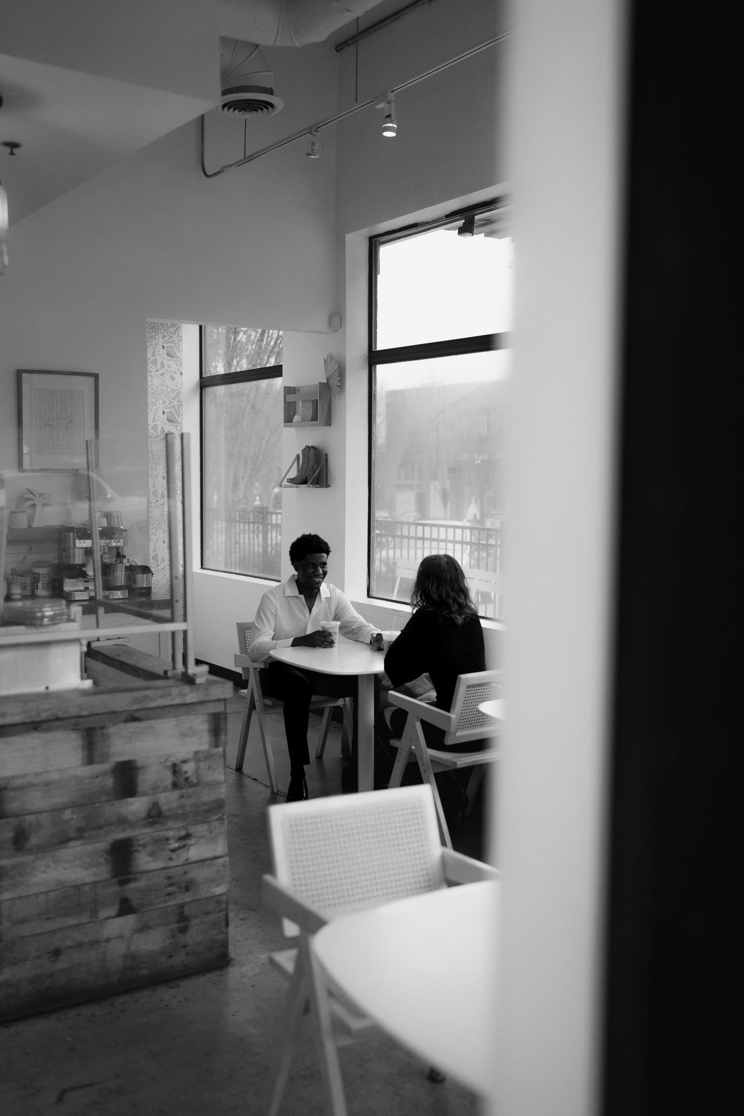 A couple sits across from each other at a cafe table in a candid black and white photo.
