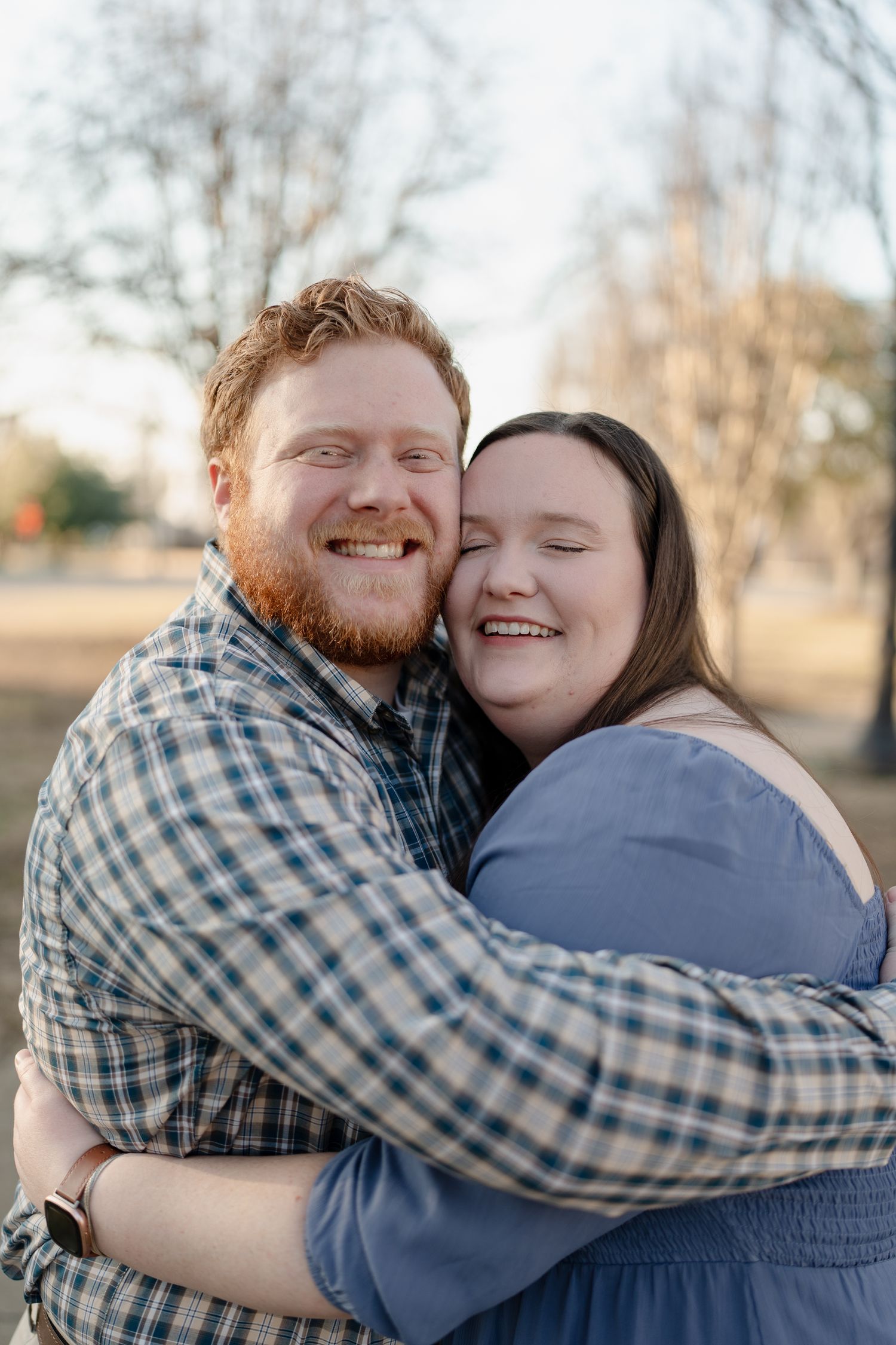 Happy couple hugging and laughing outdoors in a park during golden hour engagement photo session.