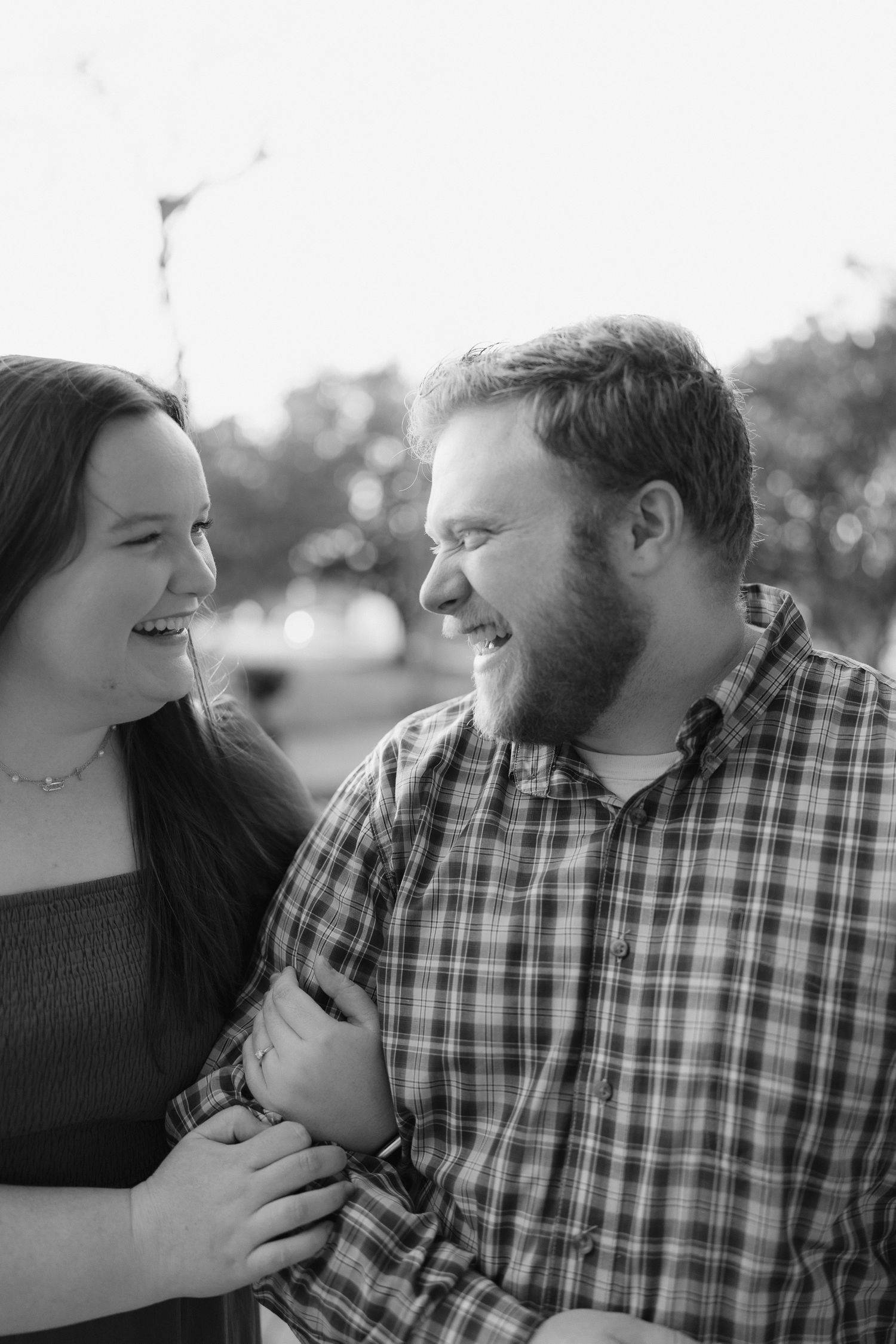 Black and white close-up of a laughing couple looking at each other outdoors with bokeh background.