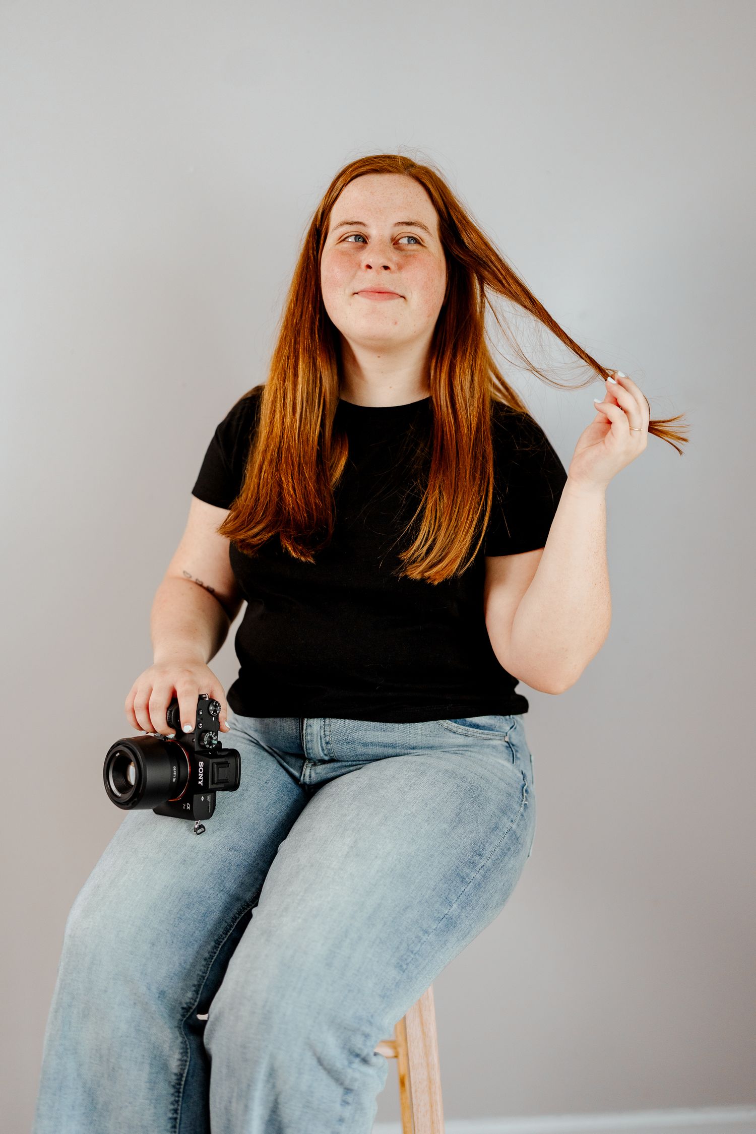 Person in black tee and jeans playfully posing with camera during indoor photoshoot.