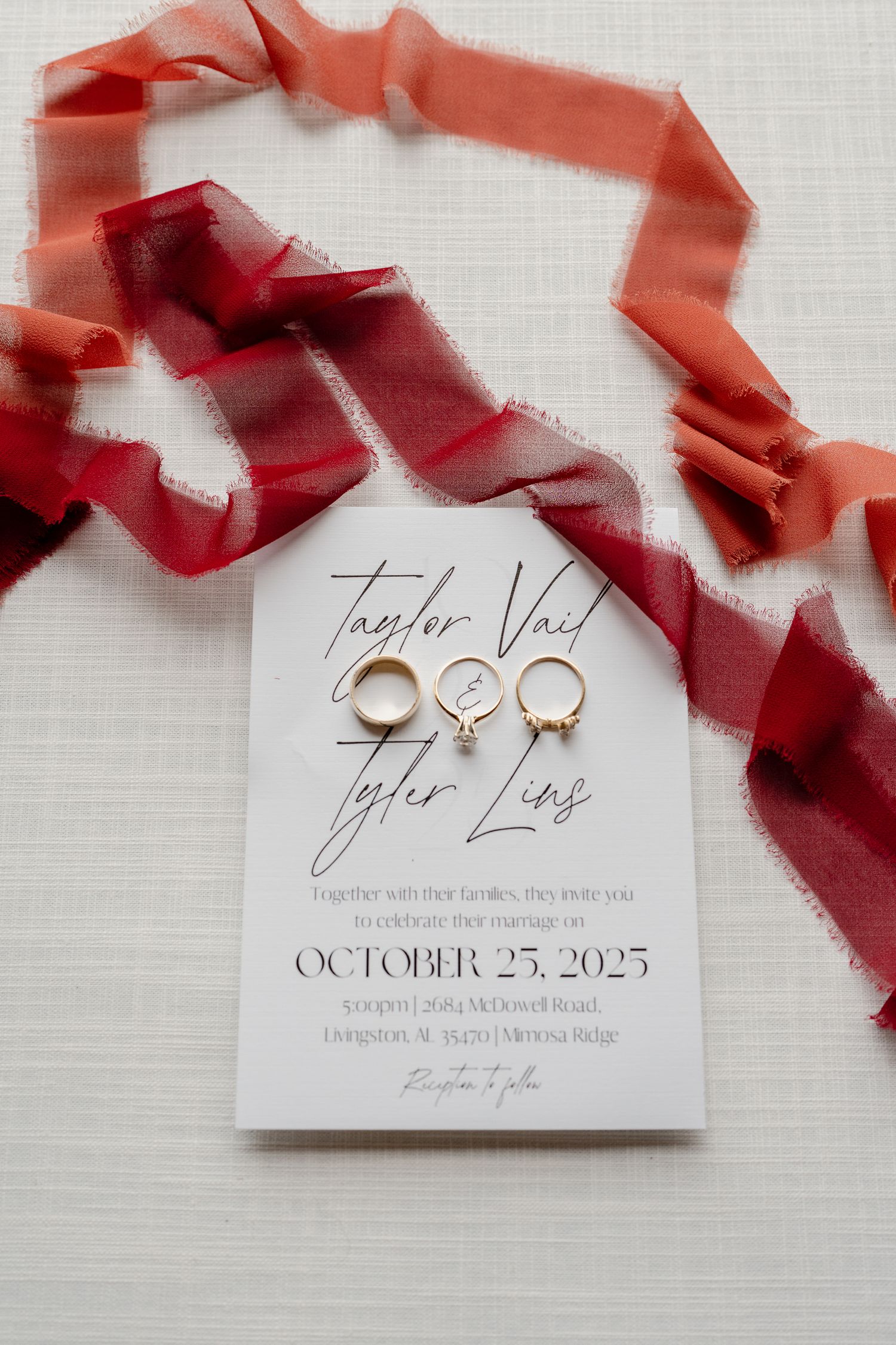 Elegant wedding invitation and rings displayed with flowing red silk ribbon on a light textured background.