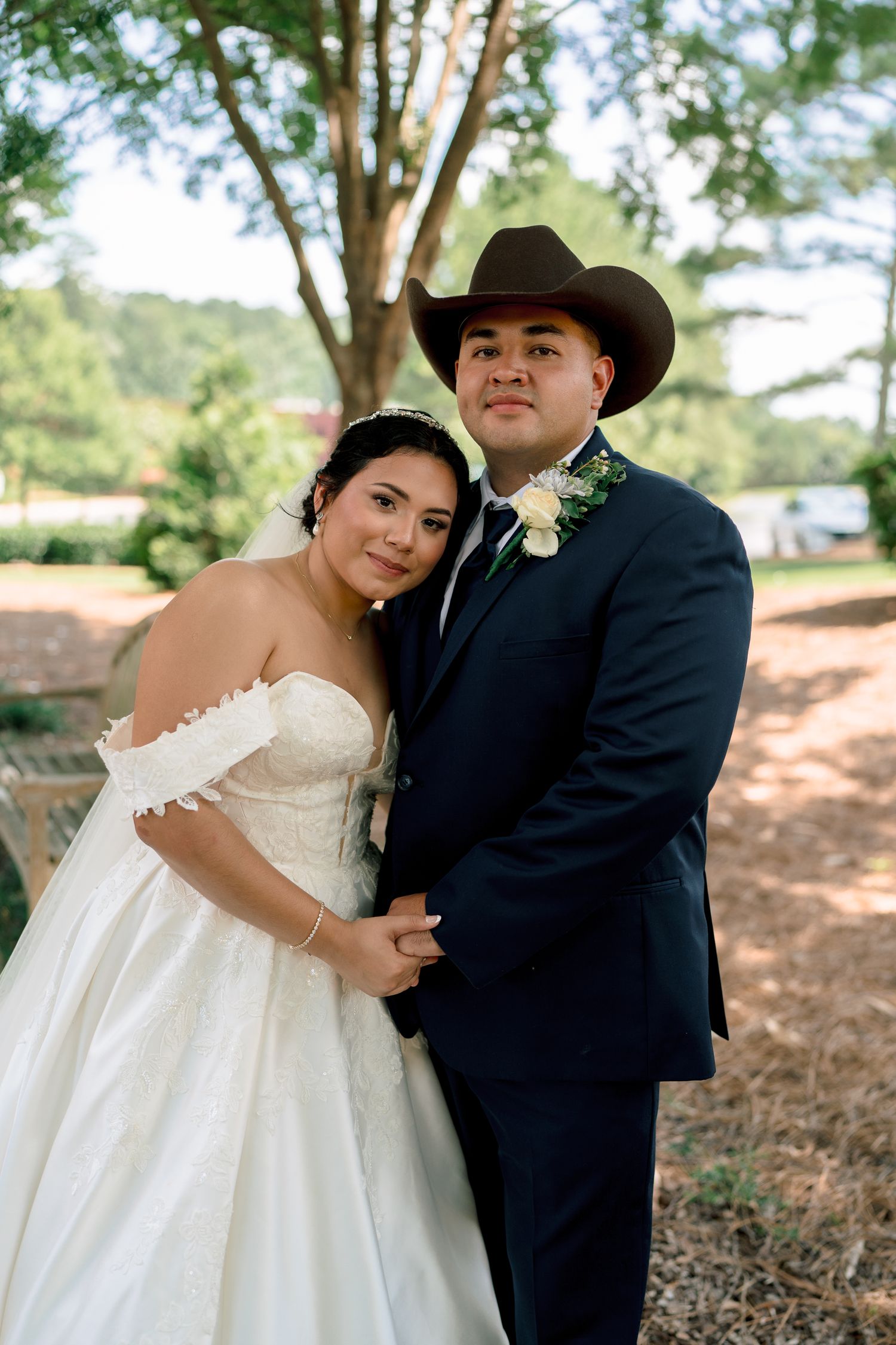 A romantic wedding couple embraces outdoors under tall trees in a natural setting.