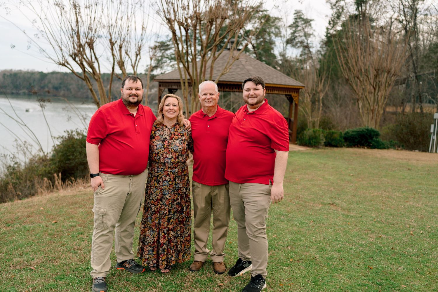 Family of four posing outdoors near a lake, wearing coordinated red and khaki outfits.