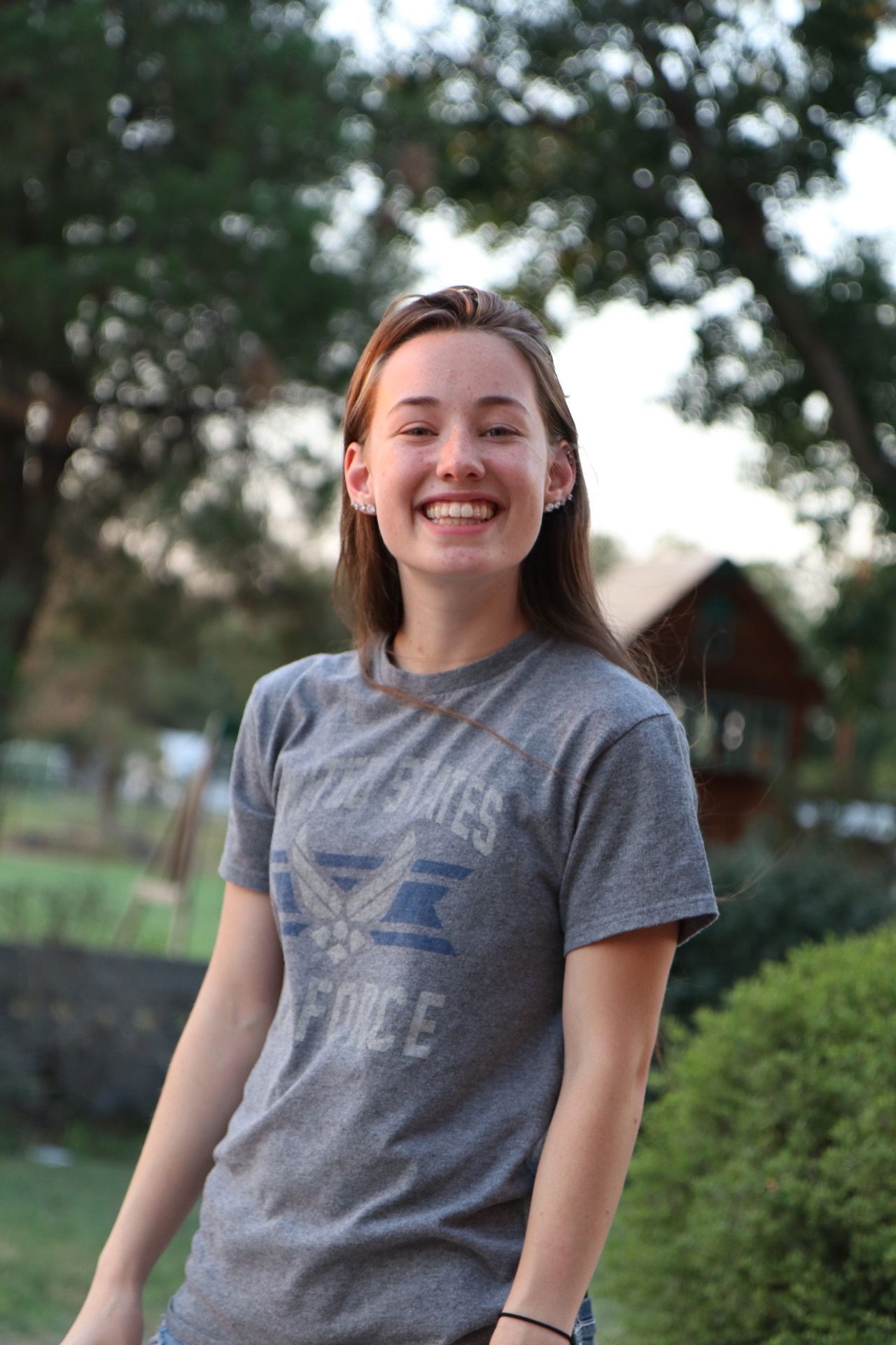 A person in a gray Air Force t-shirt smiles outdoors during golden hour.
