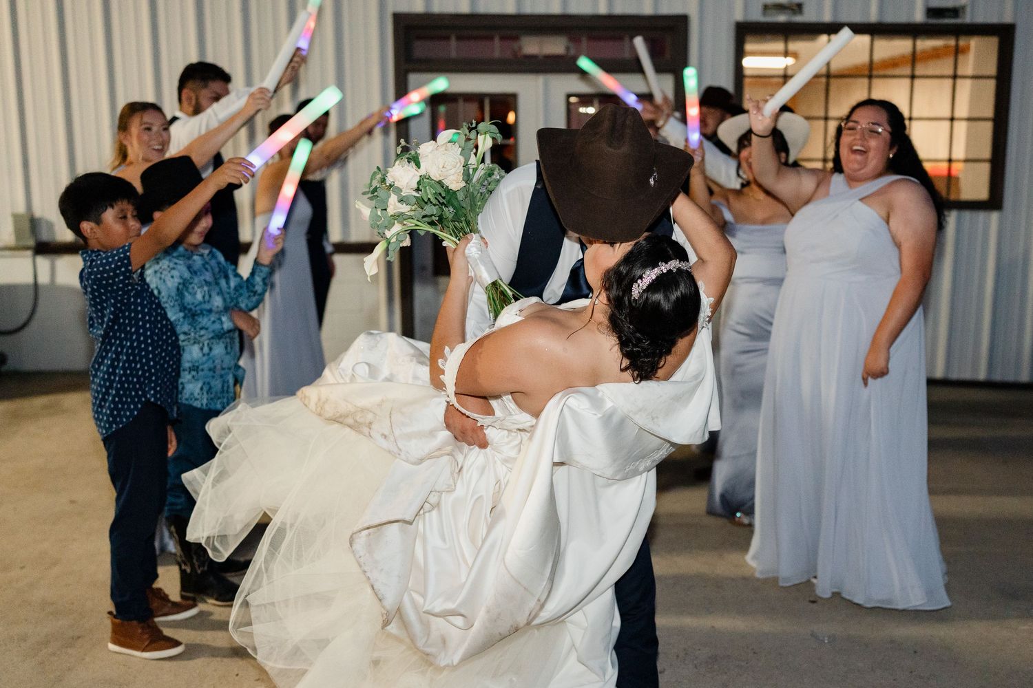 Wedding guests celebrate with light sticks while dancing at an indoor reception.