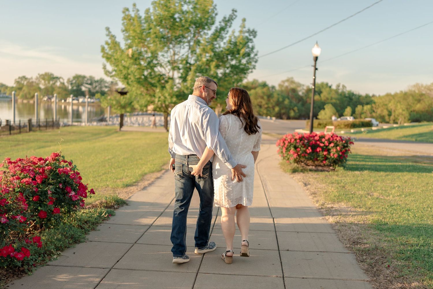 Couple walking together on pathway lined with blooming red roses and trees.