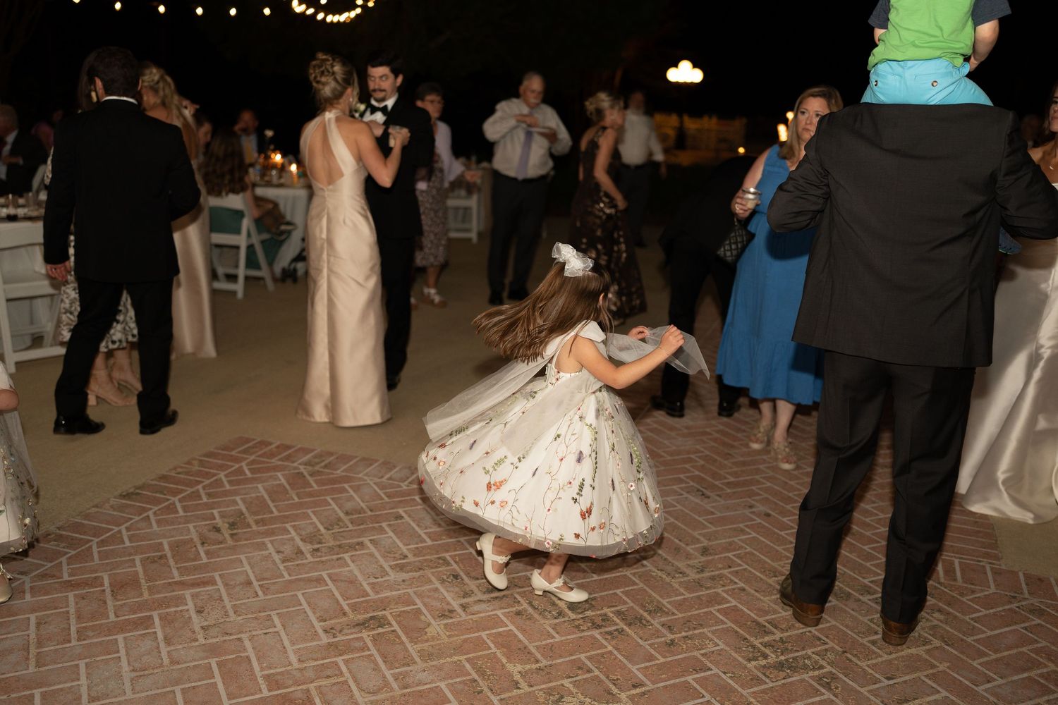 Wedding reception dance floor with string lights overhead and guests celebrating.