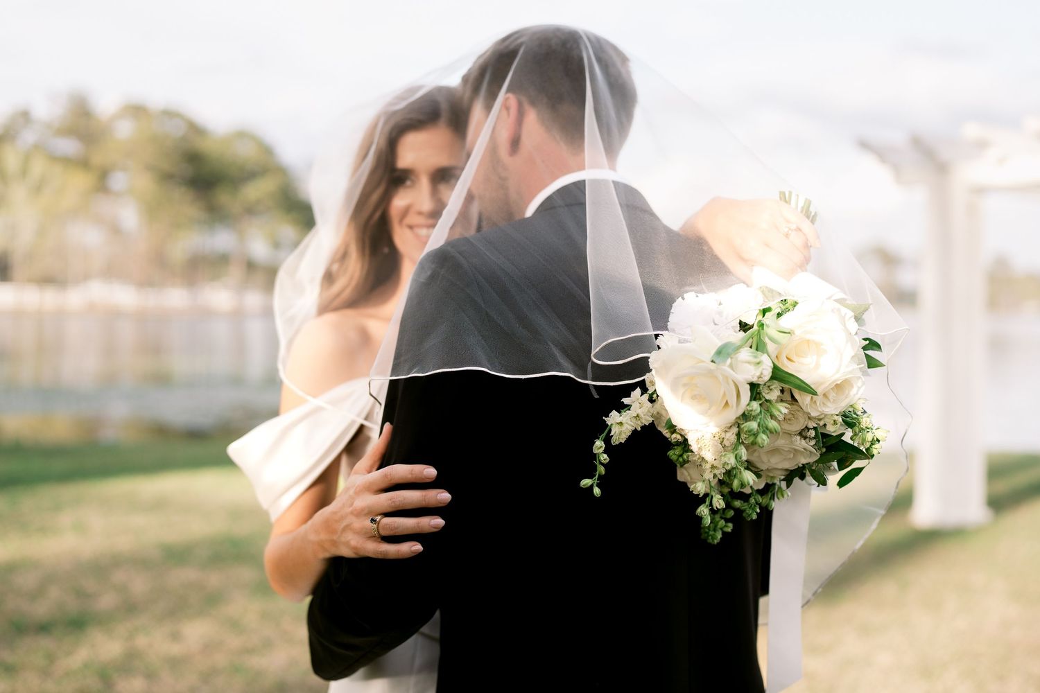 Couple shares intimate moment under veil with white bouquet in outdoor setting.