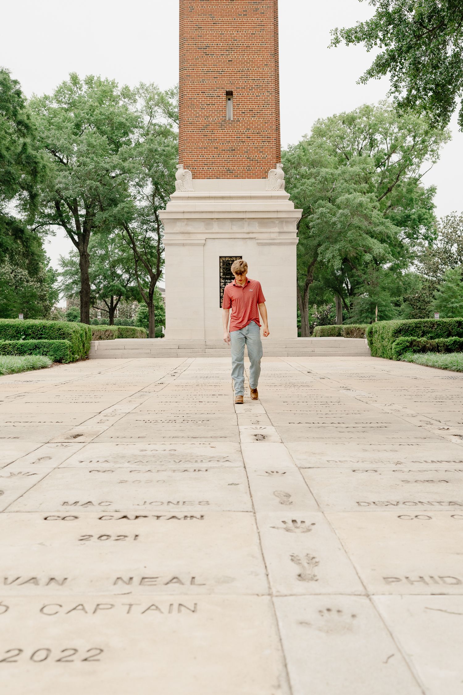 Person in coral shirt poses on engraved walkway leading to historic bell tower.